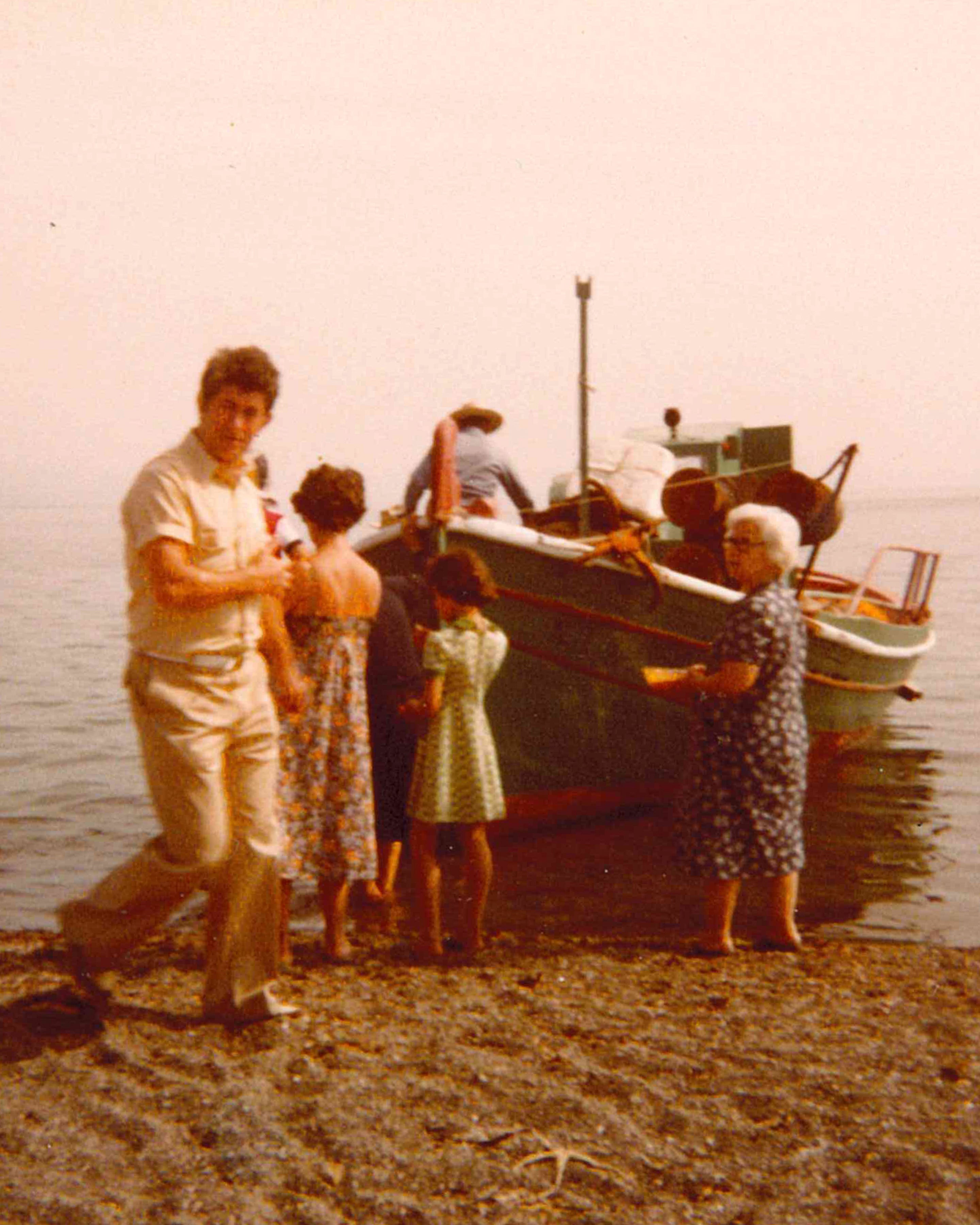 Family standing on shore in front of small boat in water