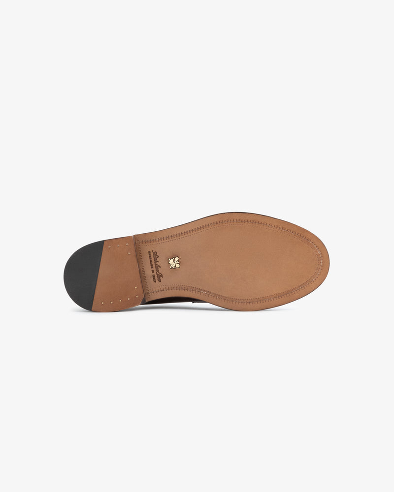 The underside of the Queens Crest Loafer, a brown leather shoe with a black heel and gold emblem near the arch.