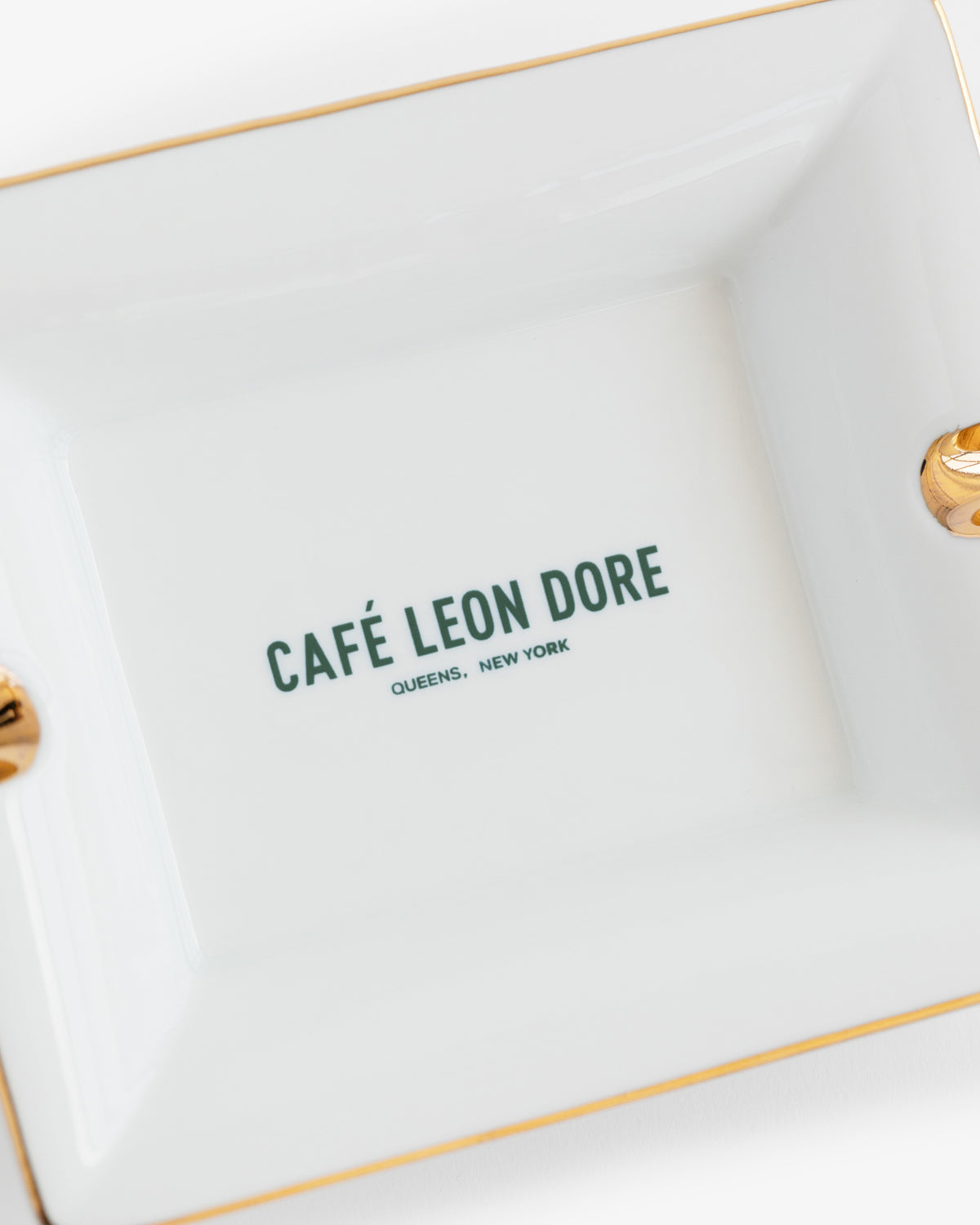 Café Leon Dore Ashtray: White porcelain with gold trim, green "CAFÉ LEON DORE QUEENS, NEW YORK" at center.