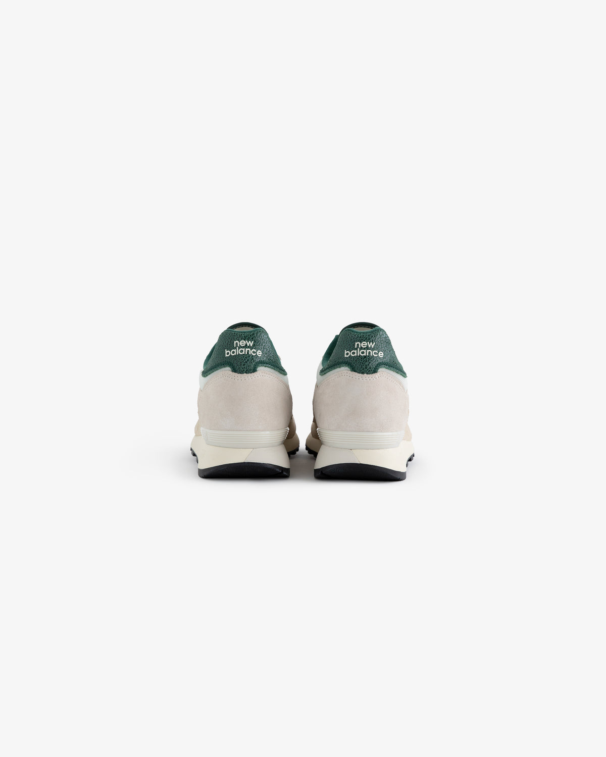 A pair of ALD / New Balance 475 sneakers viewed from the back, featuring green heel tabs and white midsoles.