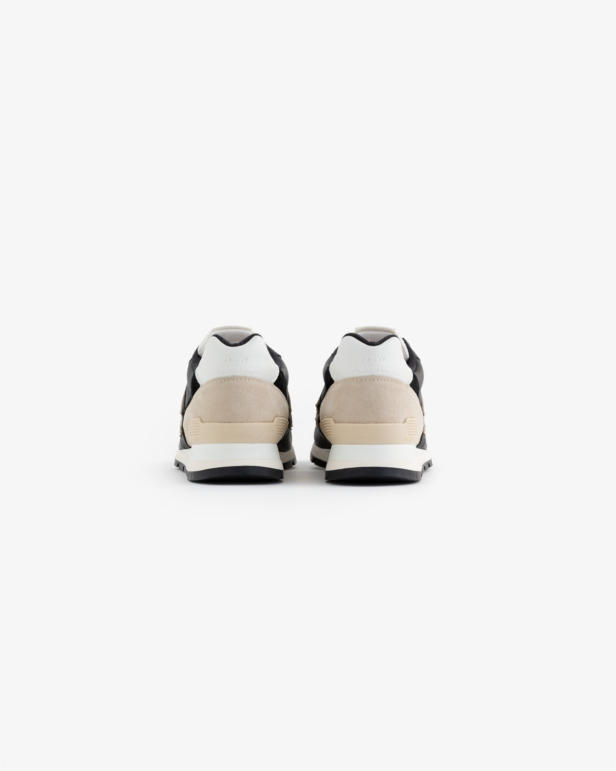 A pair of ALD / NB Made in USA 996 sneakers in black, white, and beige shown from the back on a white background.