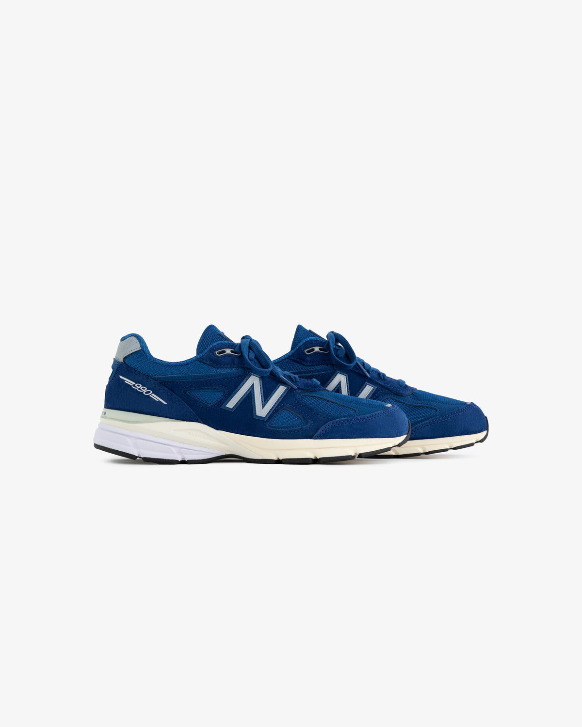 The ALD / NB Made in USA 990v4 sneakers in blue with white soles, shown from the side on a white background.