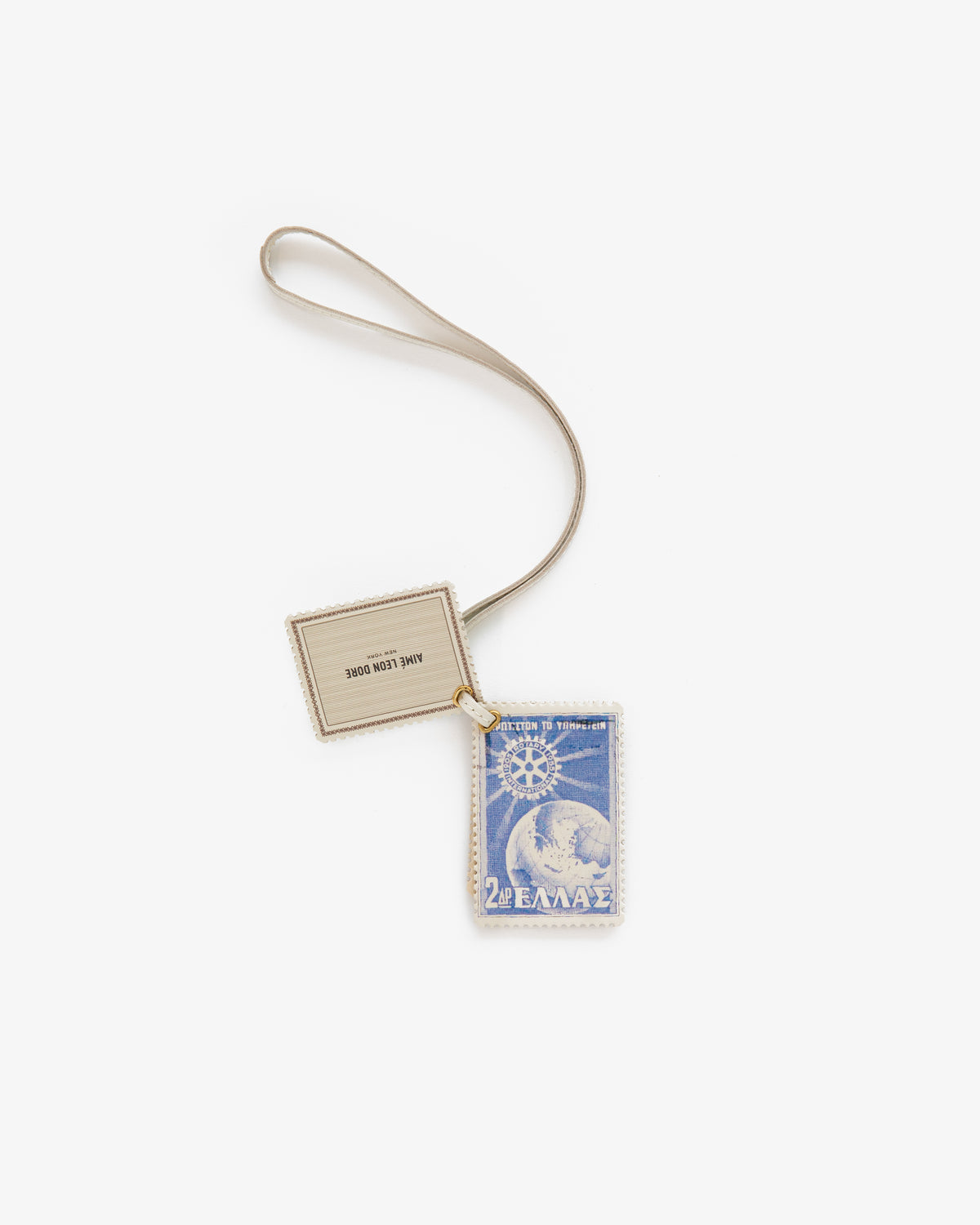 The Leather Traveler Charm is a blue postage stamp keychain with a white border and beige tag on a beige strap.