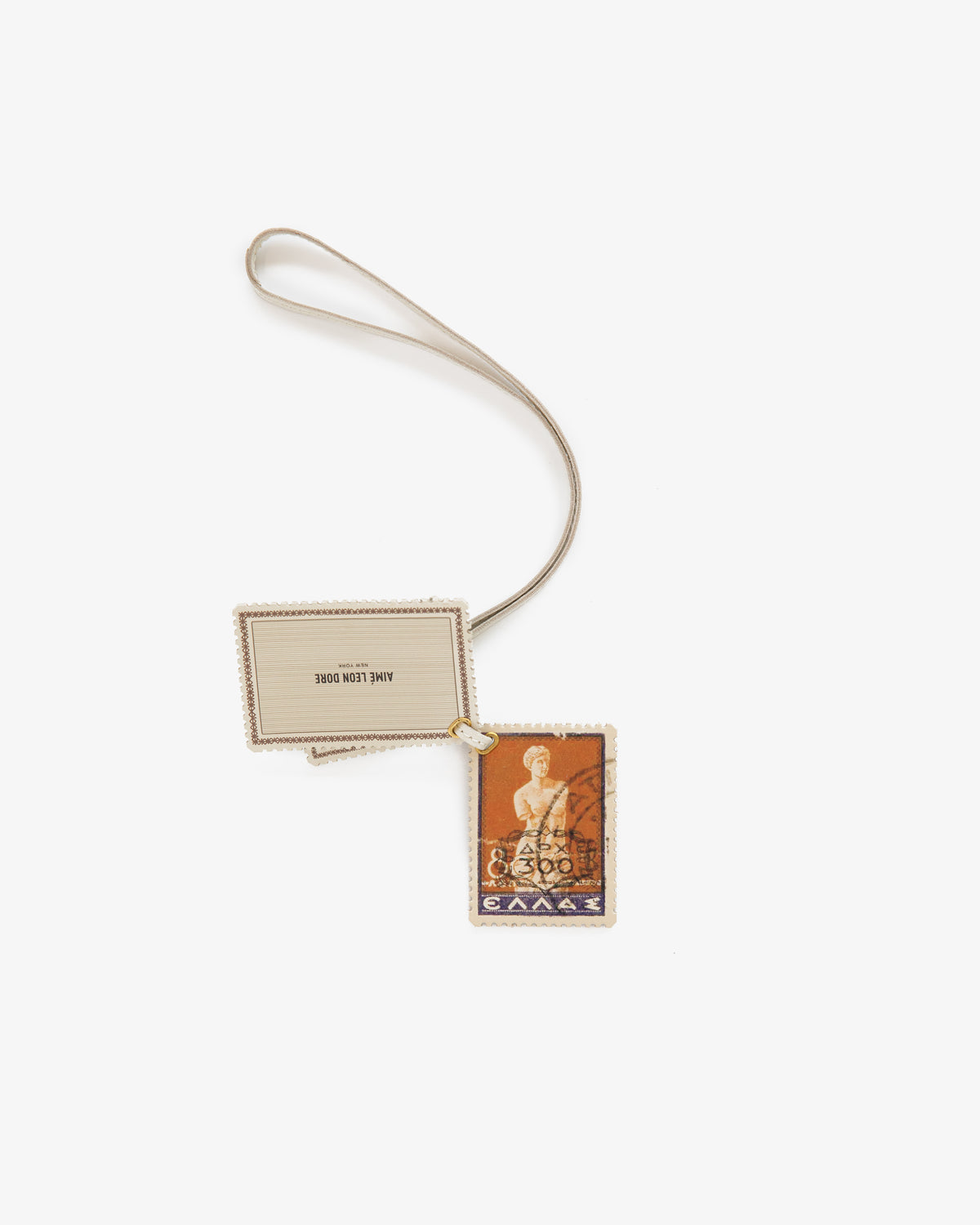 Leather Traveler Charm: Greek stamp design and blank label on a beige strap, displayed on white background.