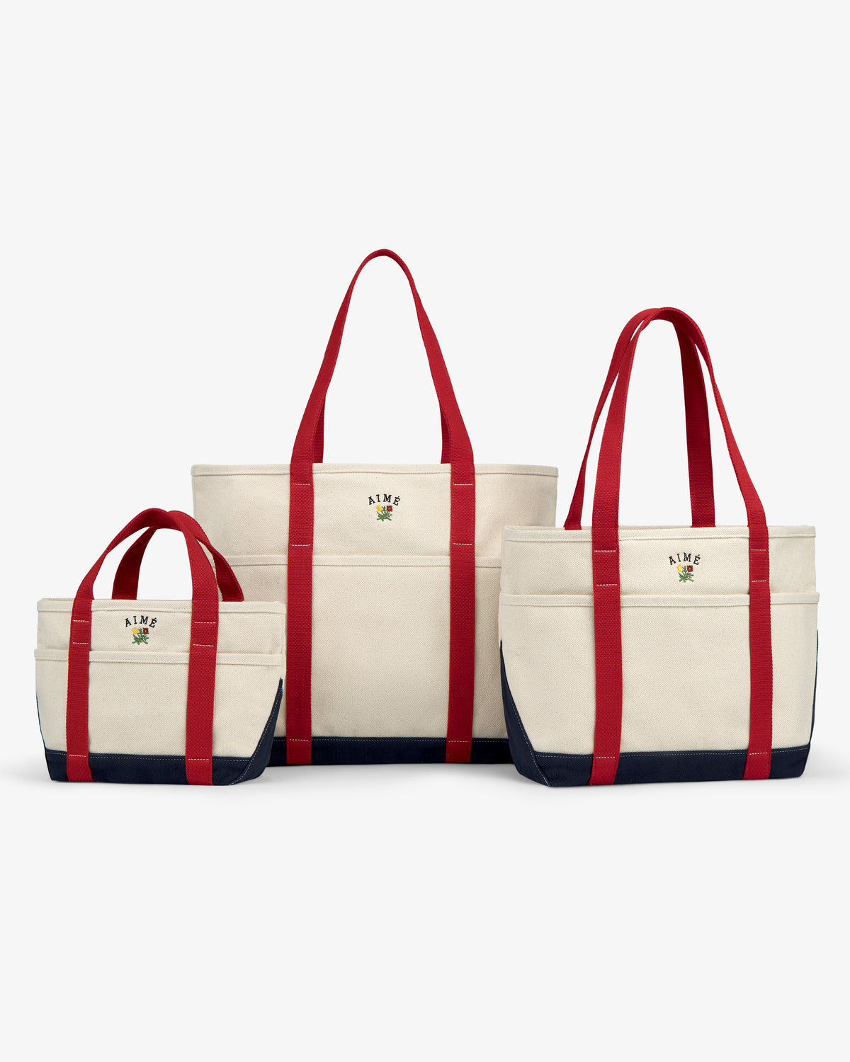 Small Crest Contrast Tote Bag shown with two other sizes, all with red handles and navy blue bottoms, side by side.