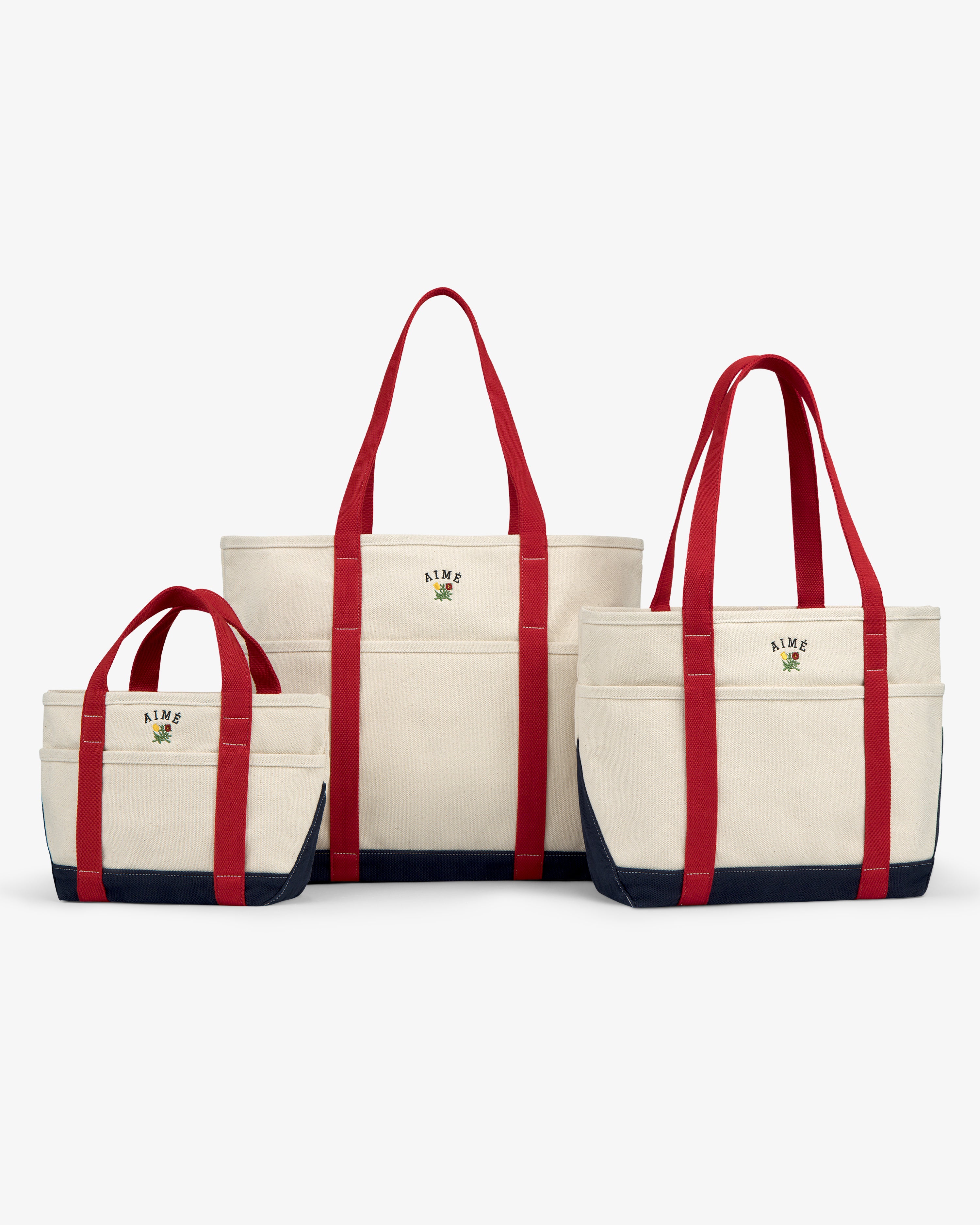 Three Mini Crest Contrast Tote Bags with red handles, navy bottoms, and logos in small, medium, and large sizes.