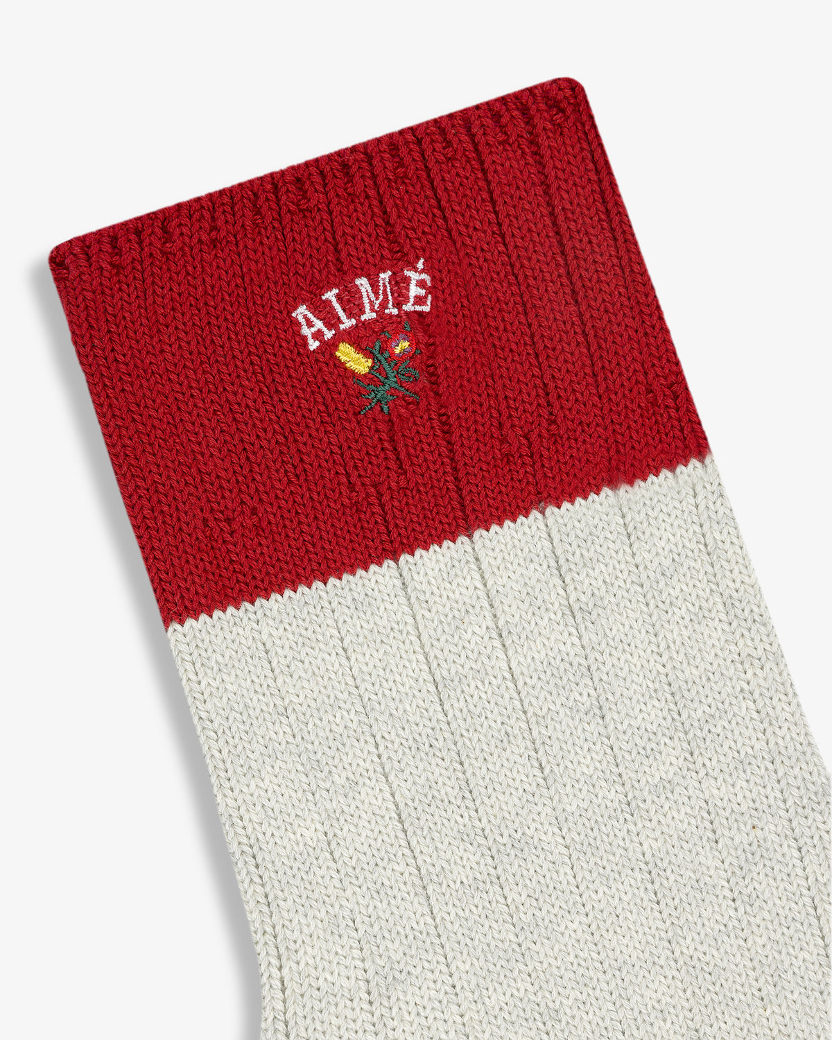 The Crest Varsity Sock is a red and white ribbed sock with AIMÉ and a small flower embroidered near the top.