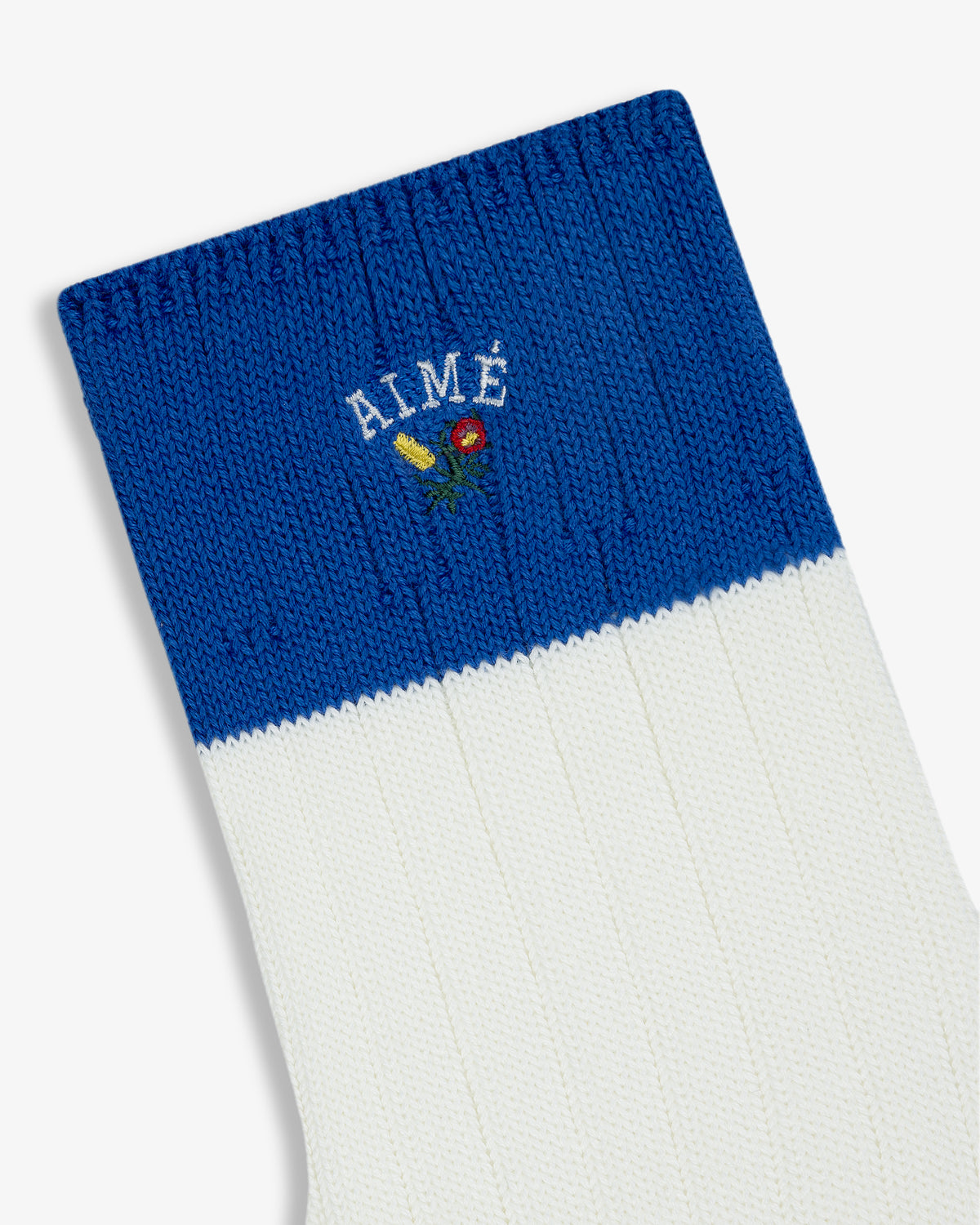 The Crest Varsity Sock is blue and white with AIMÉ and a small floral embroidered near the top.