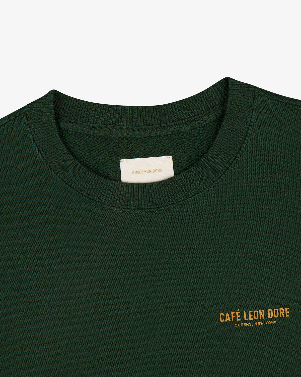 Café Leon Dore Crewneck Sweatshirt in dark green with yellow "CAFÉ LEON DORE QUEENS, NEW YORK" chest print.