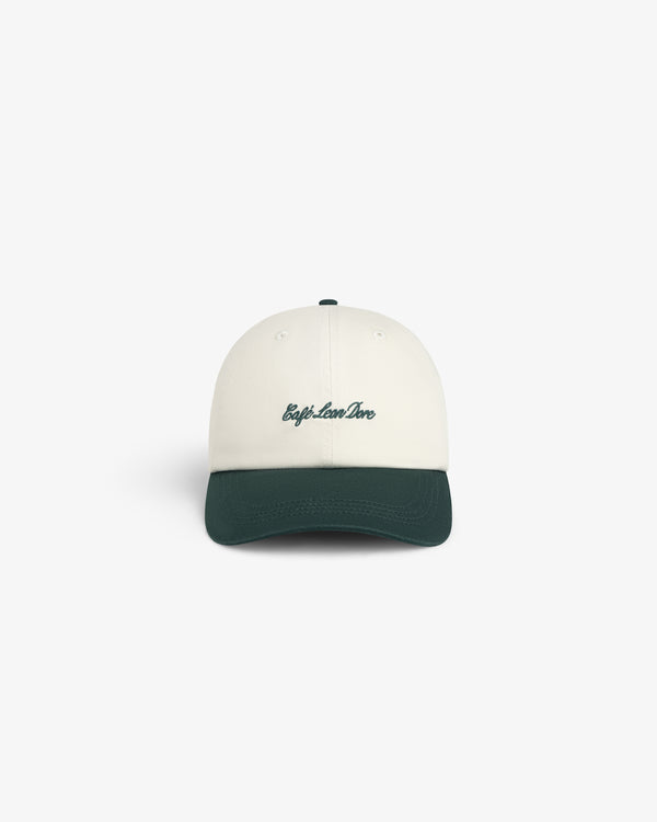 Café Leon Dore Script Hat: white cap with dark green brim, “trip.love.live” in green on front, white background.