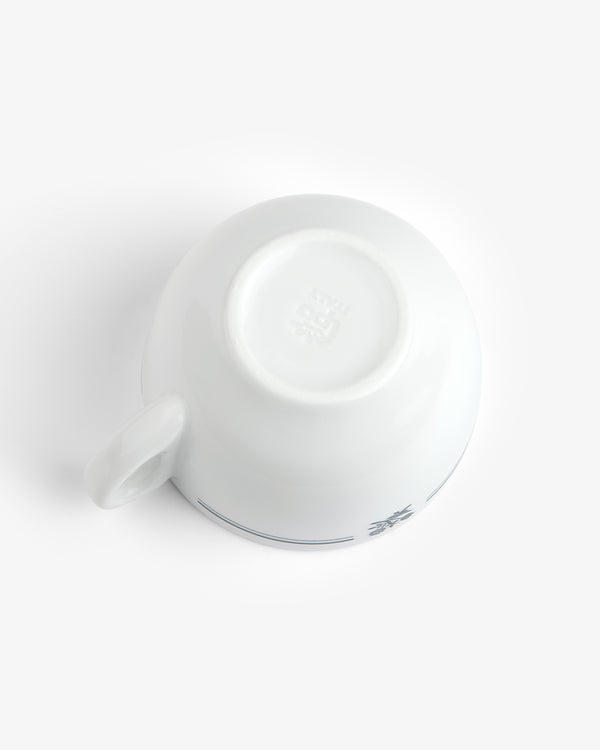 Café Leon Dore Cappuccino Cup & Saucer set, white ceramic cup upside down, handle shown left, plain background.