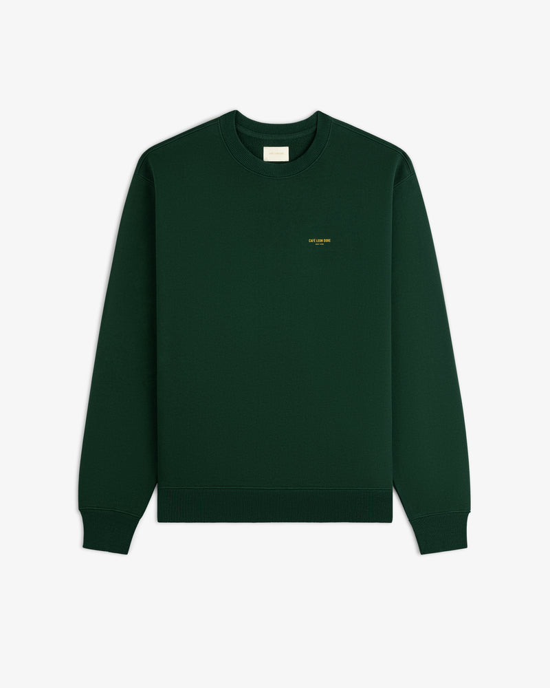 Café Leon Dore crewneck sweatshirt in dark green with small yellow left chest text, laid flat on white background.