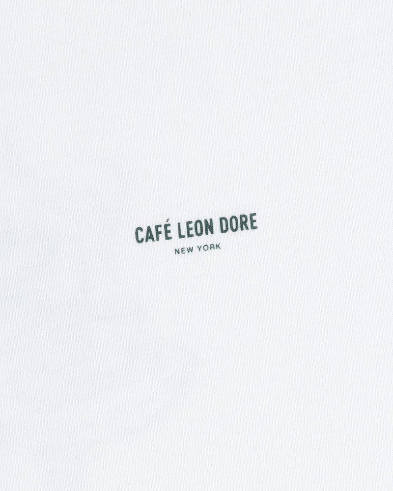 White Café Leon Dore Caricature Tee featuring small, dark “CAFÉ LEON DORE NEW YORK” print at the center.