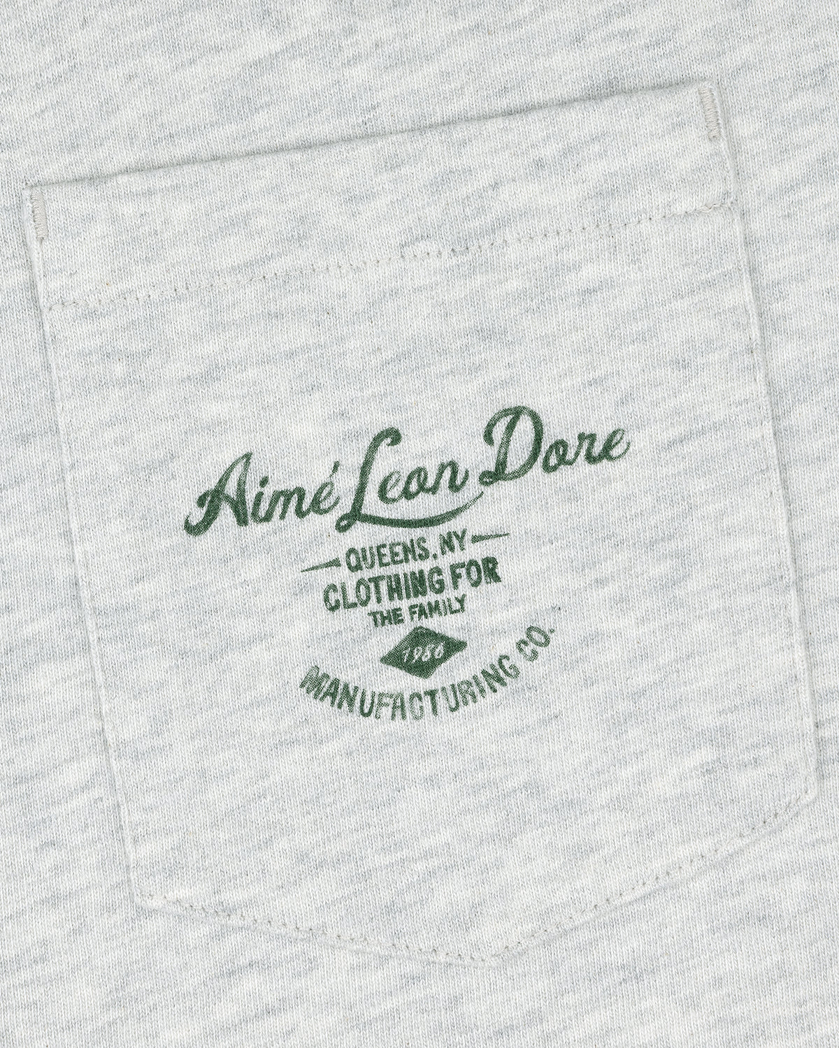 Light gray General Store Pocket Tee with dark green text: "Aimé Leon Dore Queens, NY Clothing For The Family 1986 Manufacturing Co.