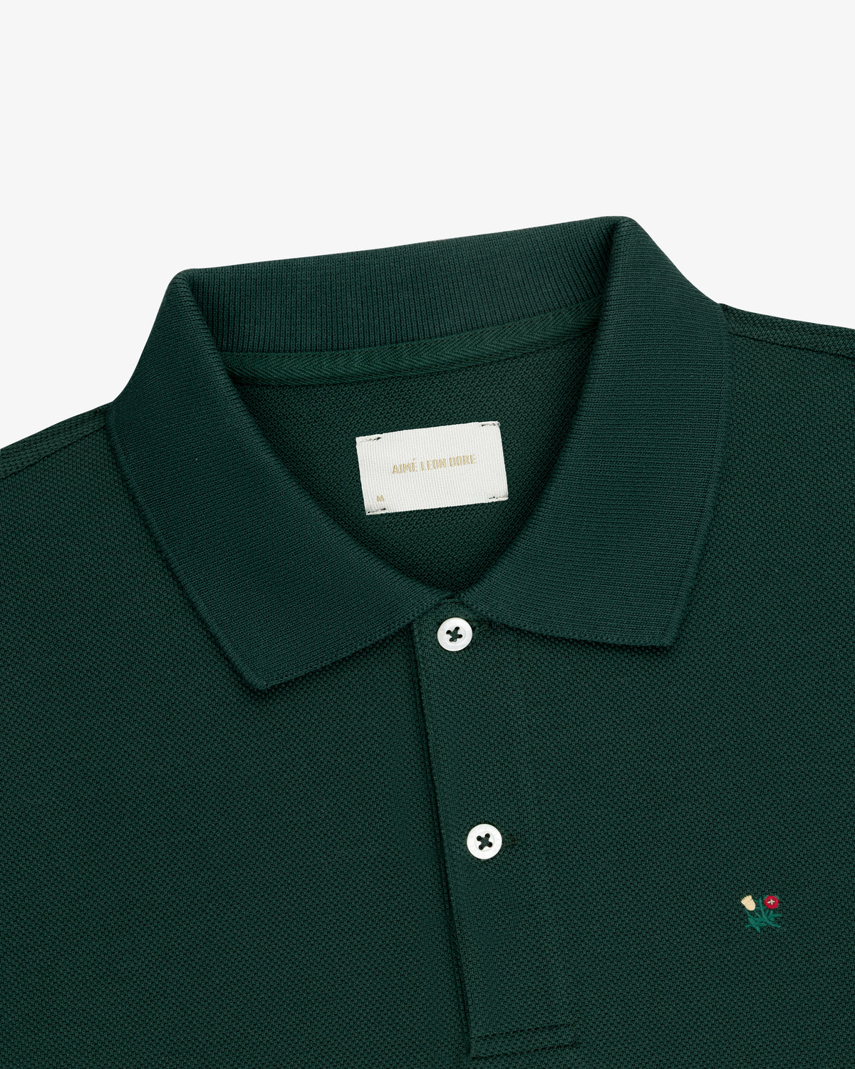 Crest Piqué Polo in dark green with a collar, two white buttons, and red & yellow chest embroidery.