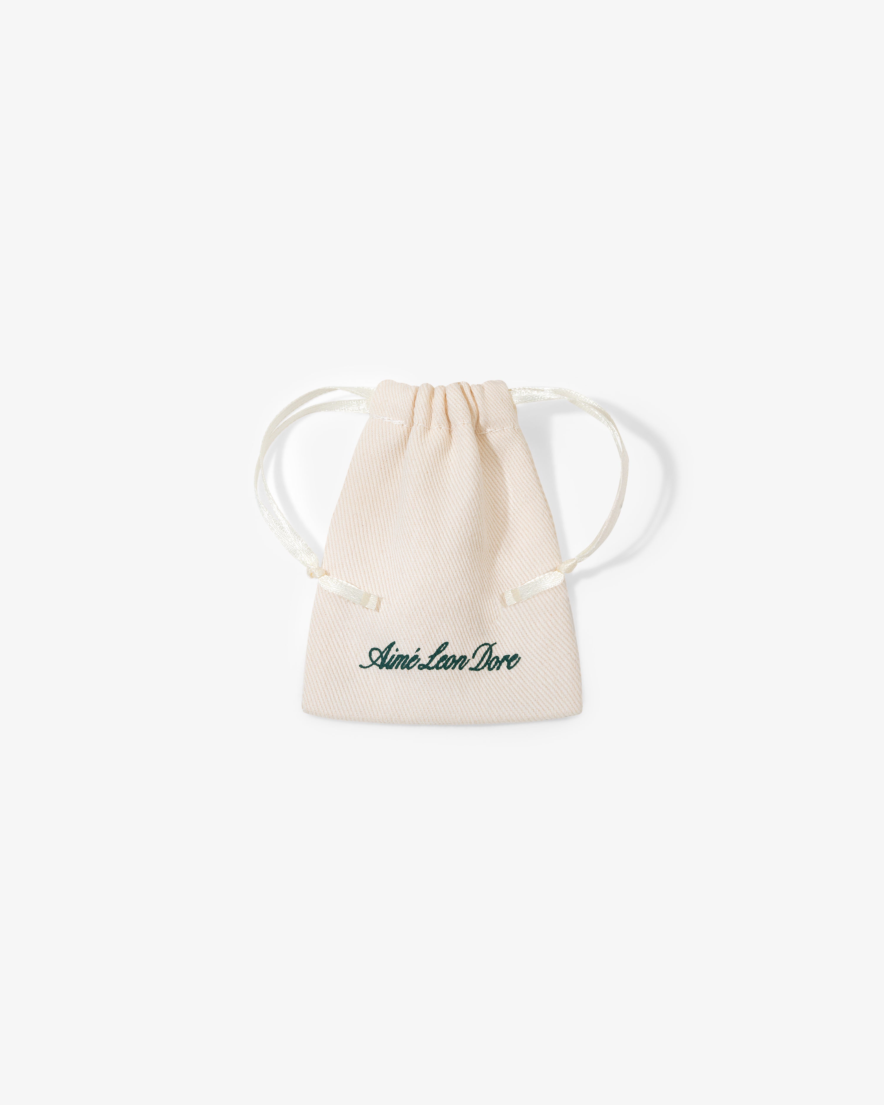 A small beige drawstring pouch with "Queens Crest Penny" written in green script on the front.