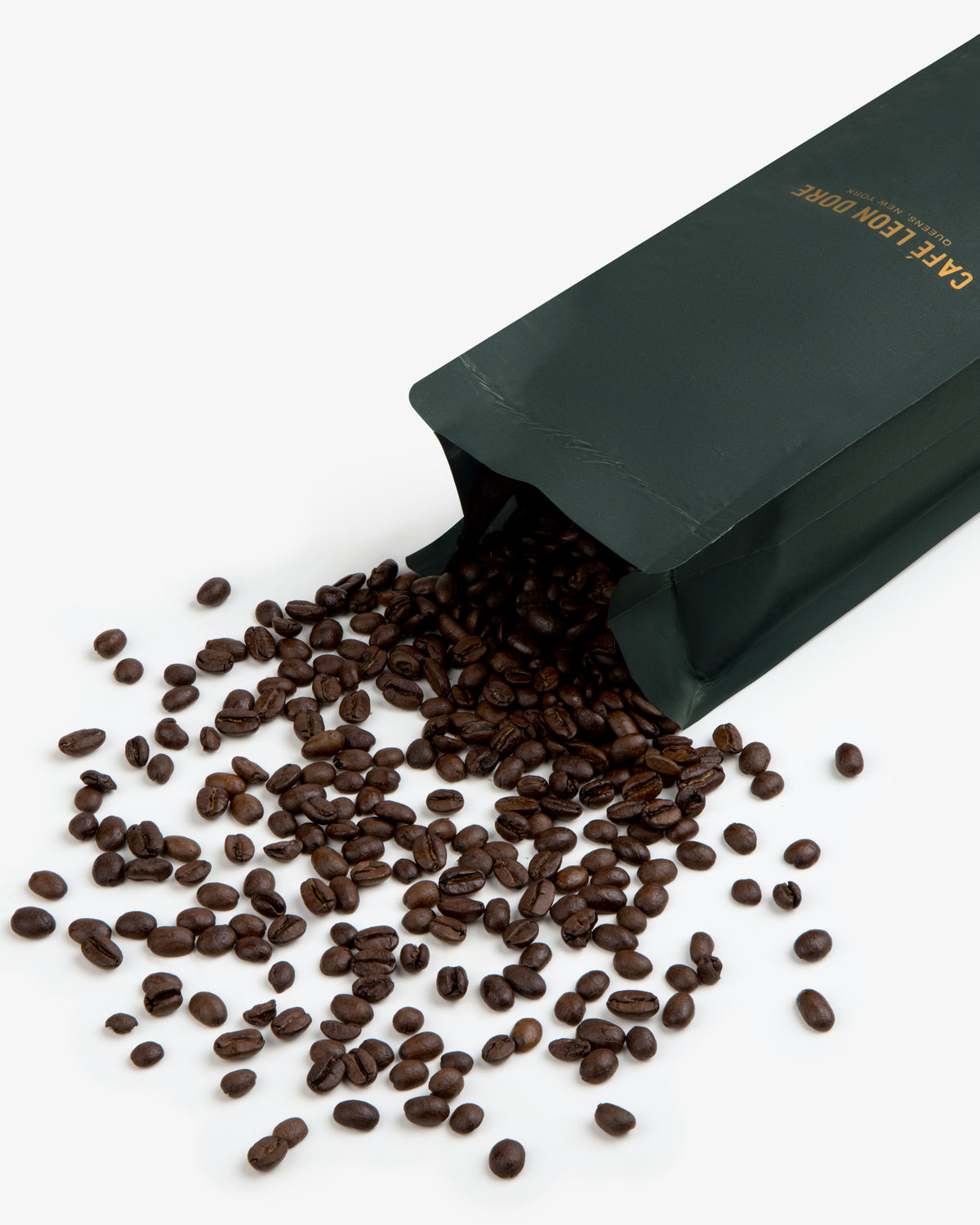 A bag of ALD Espresso Beans spills roasted coffee beans onto a white surface.