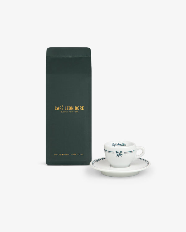 A dark green ALD Espresso Beans bag next to a white espresso cup and saucer on a white background.