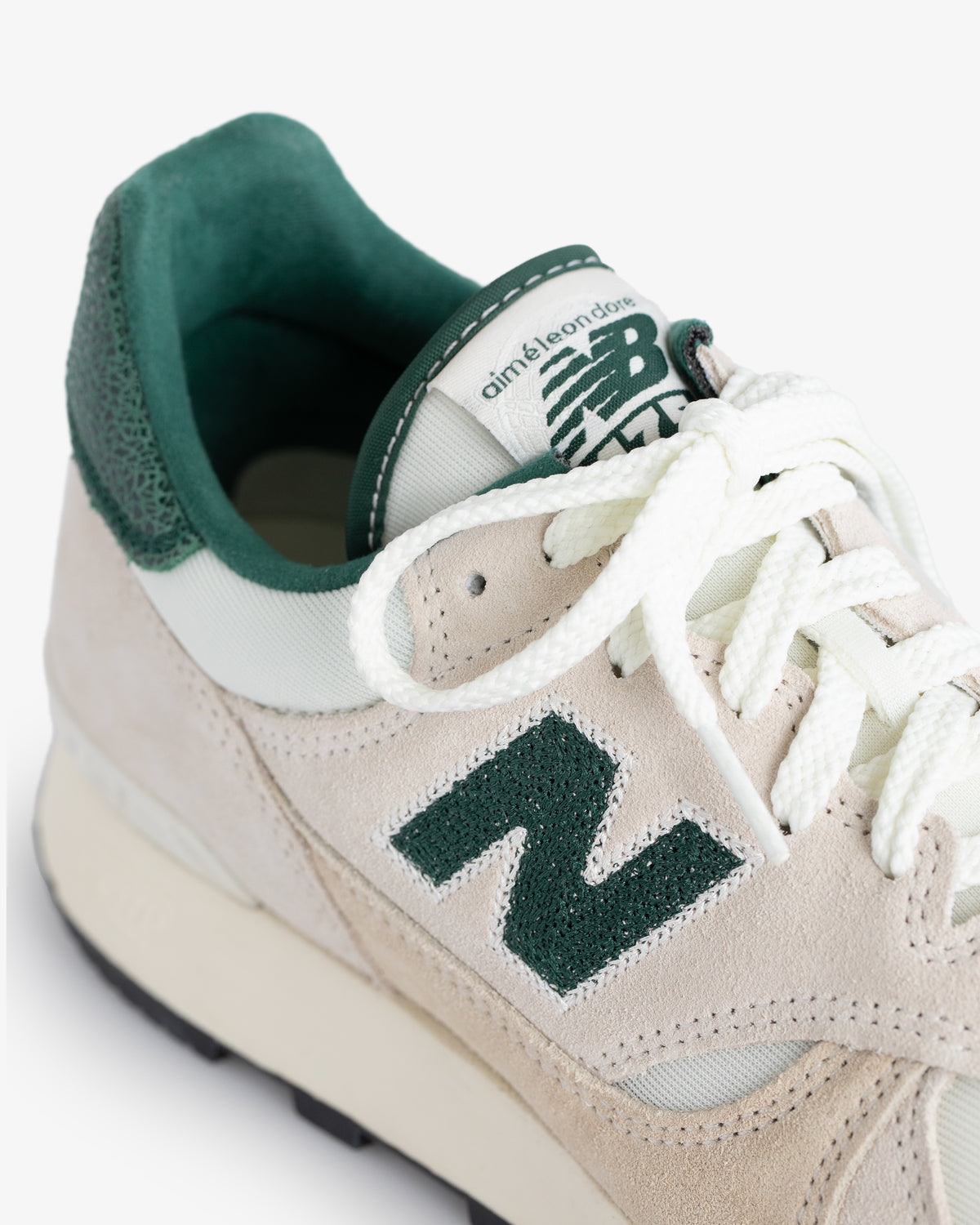 Close-up of an ALD / New Balance 475 sneaker in beige and green with white laces and suede accents.