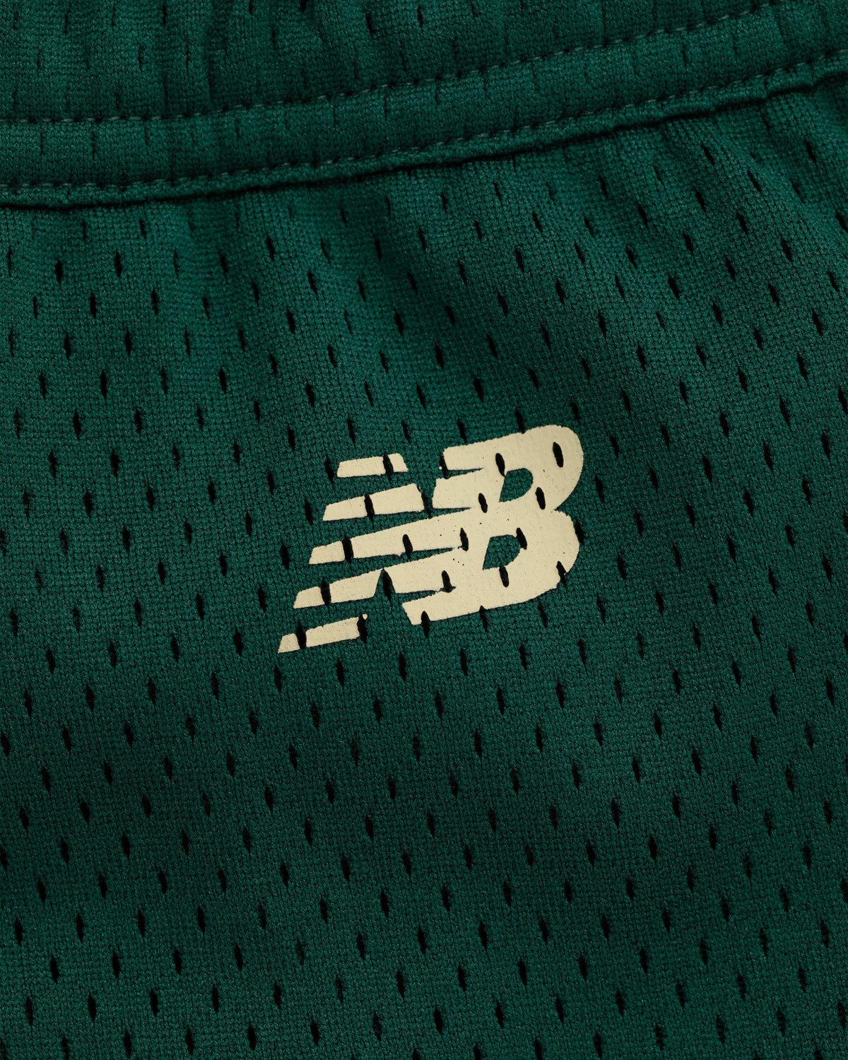 Close-up of a white New Balance logo on green mesh ALD / New Balance SONNY NY Gym Short.