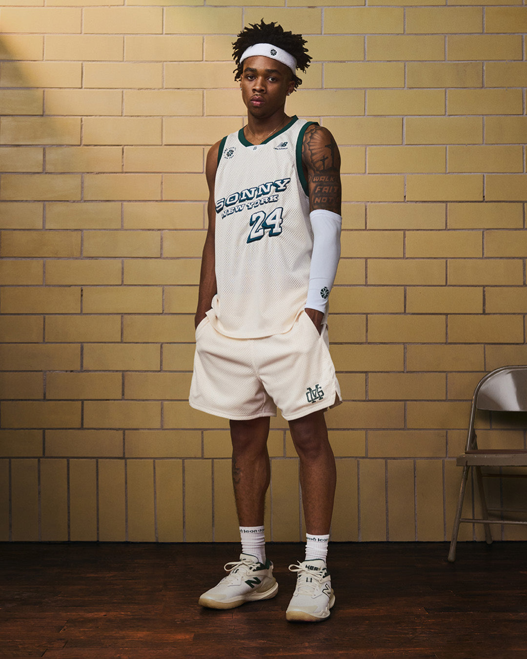 Basketball player wears ALD/New Balance SONNY NY IFTB Jersey indoors by brick wall, looking at the camera.