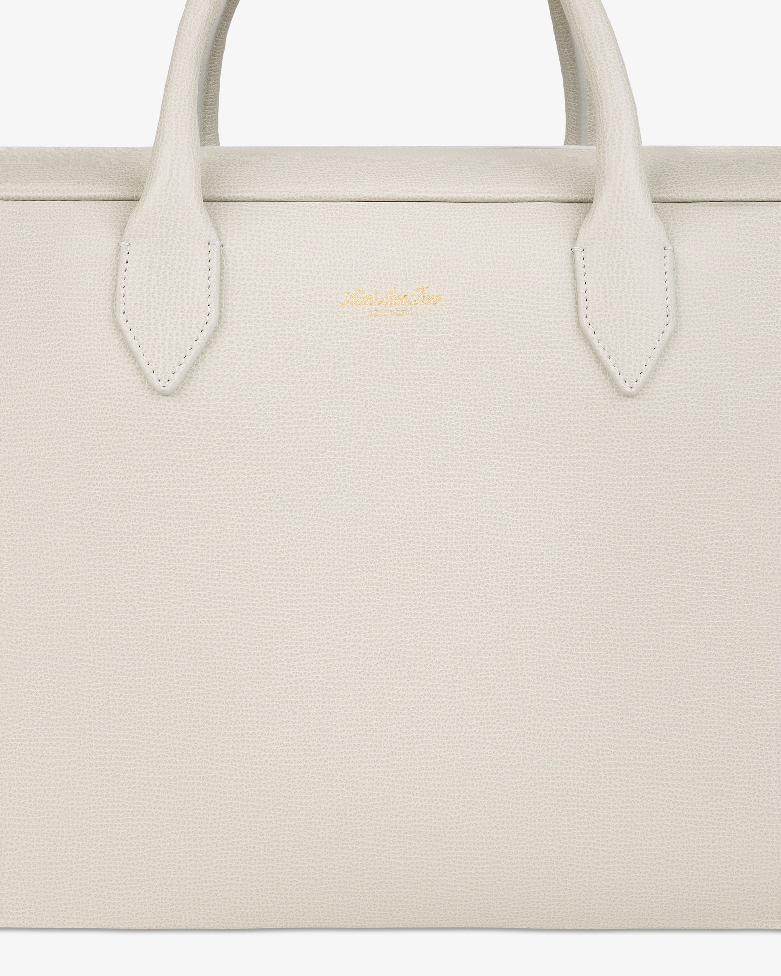 Close-up of a textured, off-white Full Grain Leather Briefcase Duffle with two handles and a small gold logo in the center.