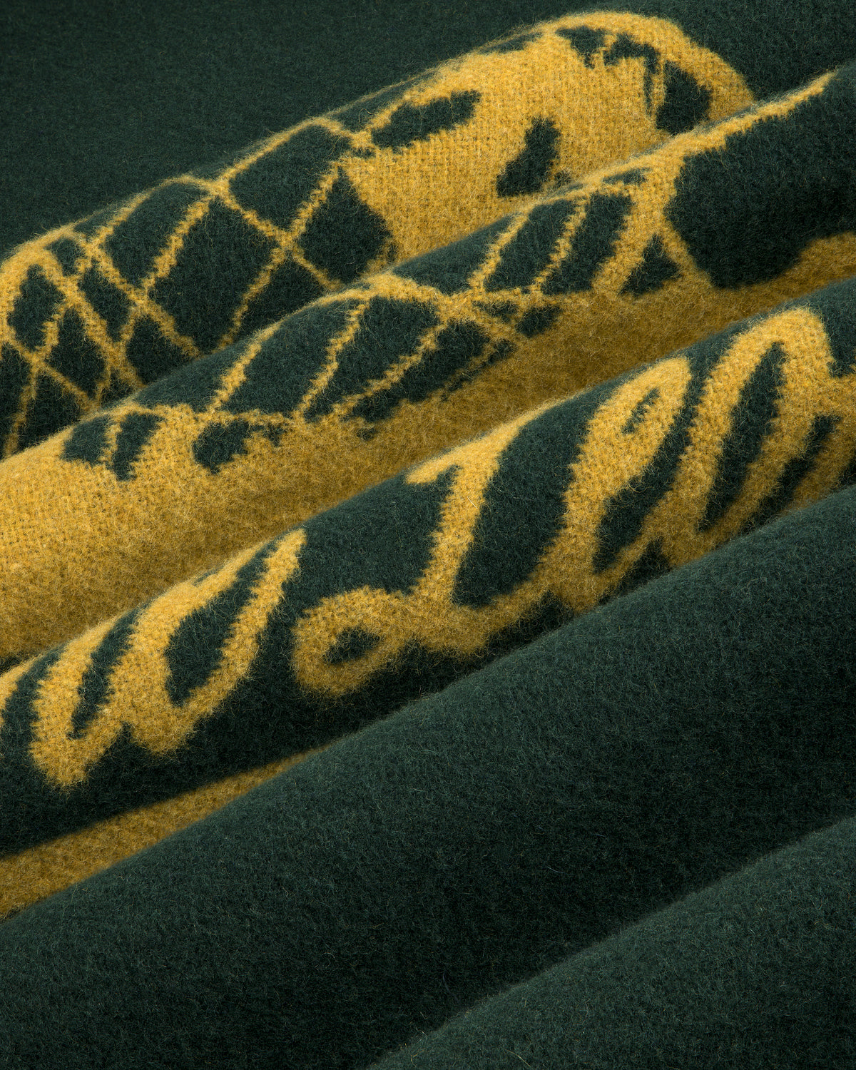 Close-up of the Unisphere Wool Blanket, featuring soft folded fabric with green and yellow script and diamond patterns.