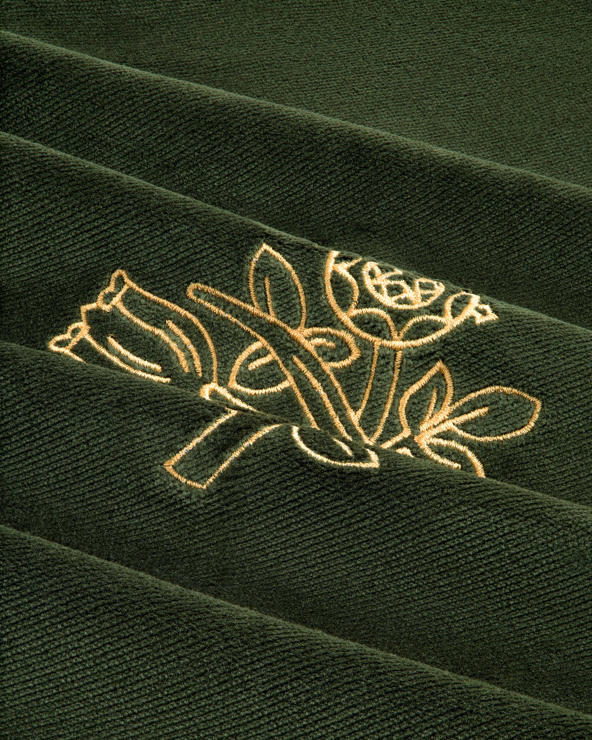Close-up of the Queens Crest Throw Pillow's green fabric with two flowers and leaves embroidered in light yellow thread.