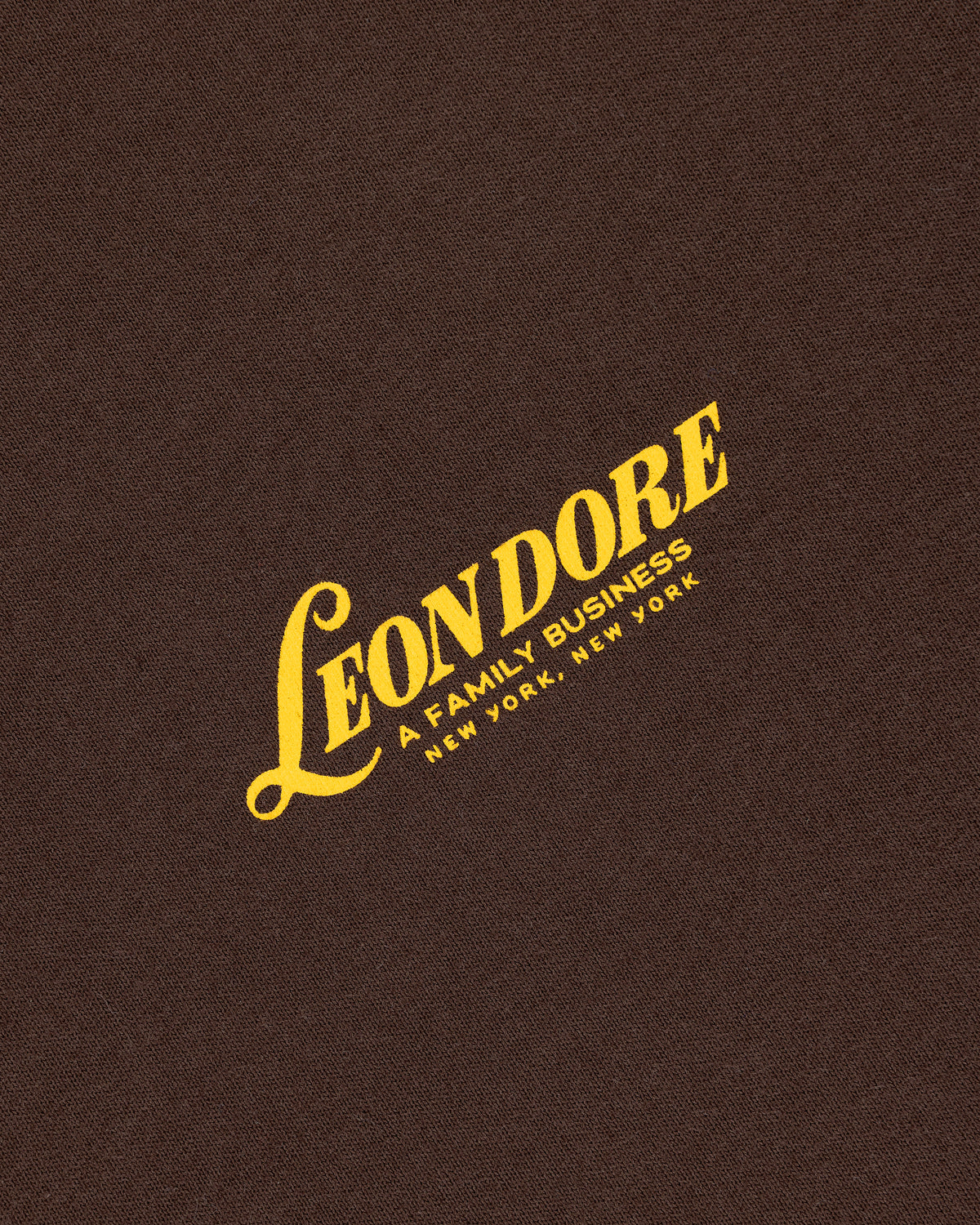 Yellow "LEON DORE, A FAMILY BUSINESS, NEW YORK, NEW YORK" text on brown textured Leon Dore Tee.