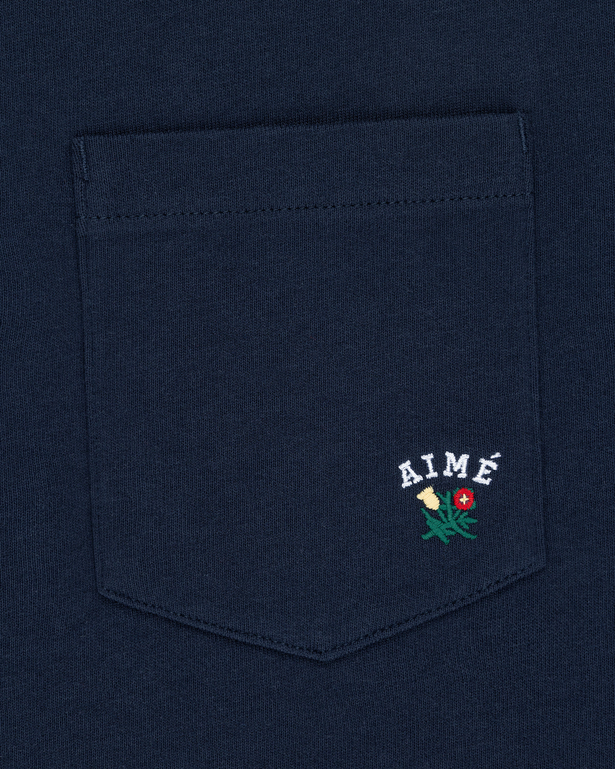 Navy Crest Pocket Tee with “AIMÉ” text and small embroidered flower design below the lettering.