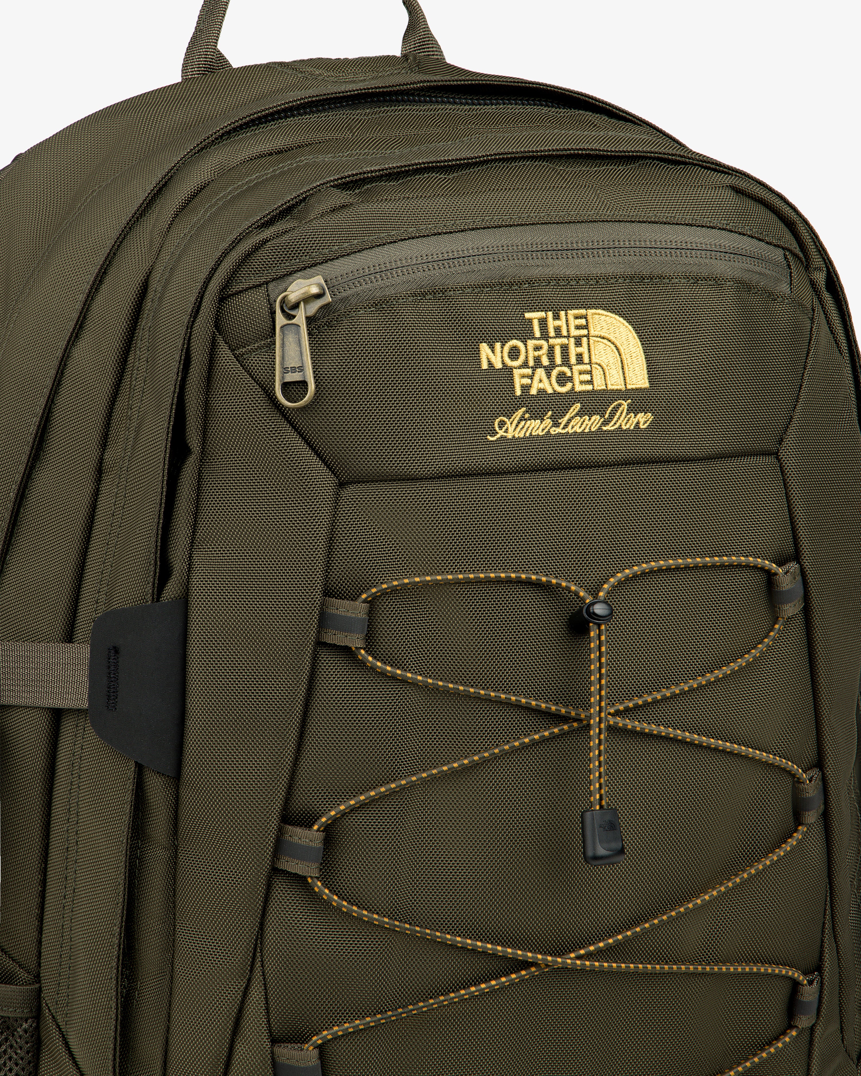 Olive green ALD/The North Face Borealis Backpack with yellow logo, front zipper pocket, and yellow bungee cord.