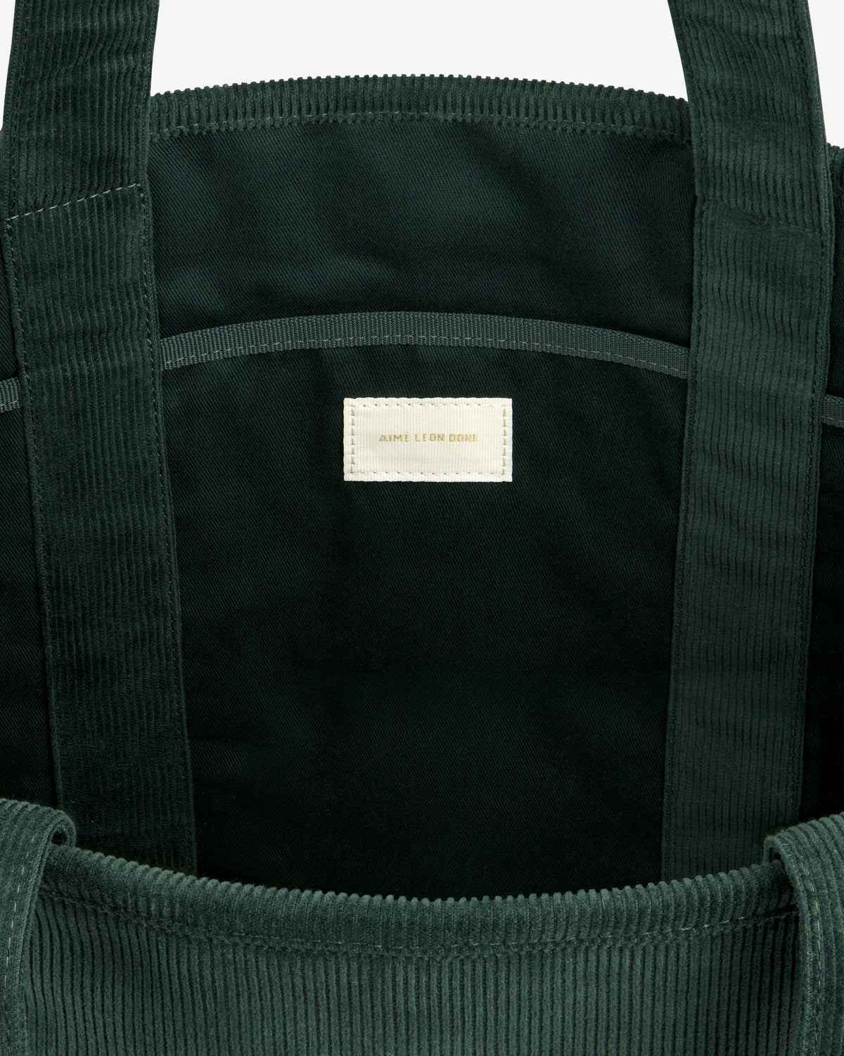 Interior of a dark green Large Corduroy Unisphere Tote Bag featuring a central fabric label with gold lettering.