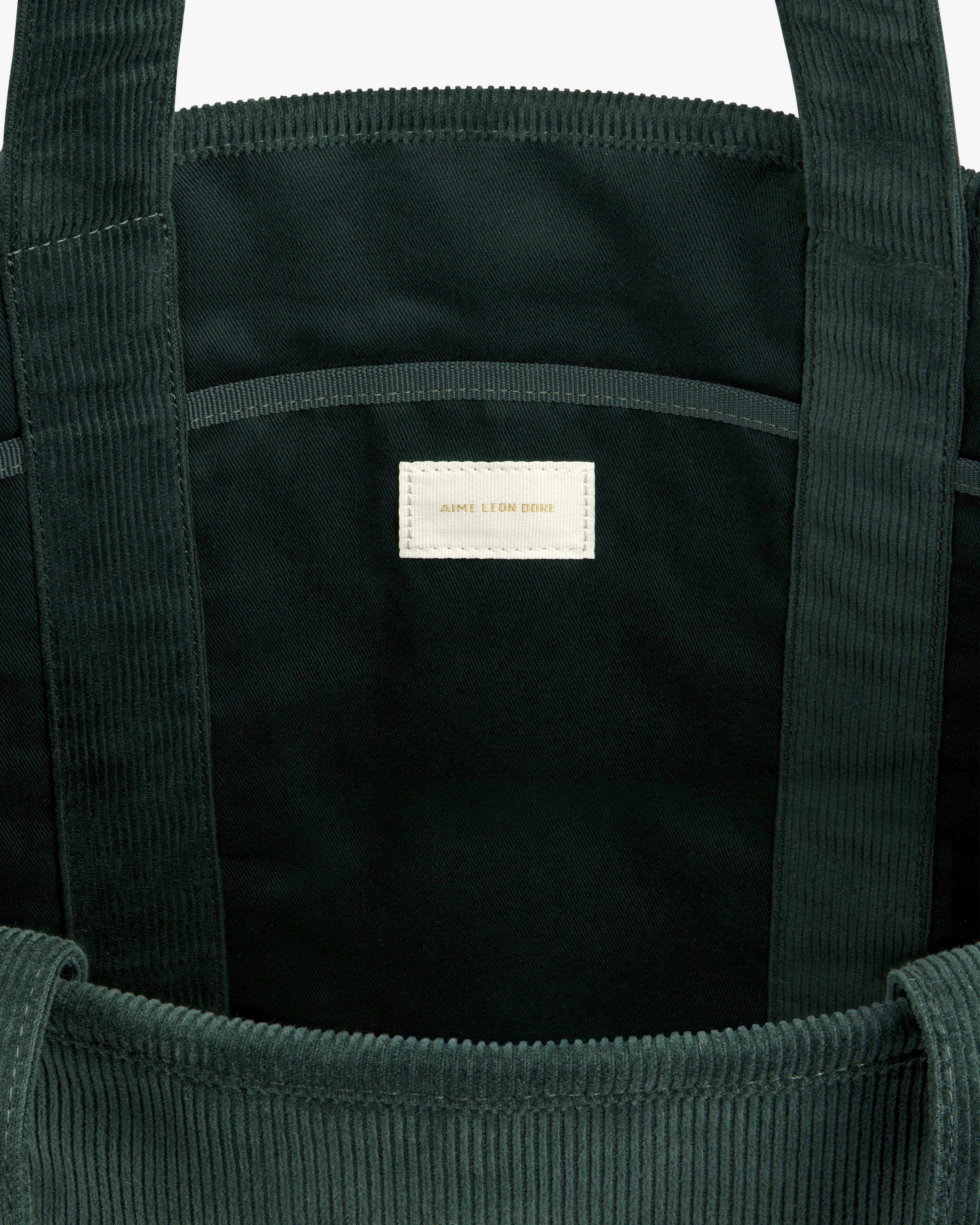 Interior of a dark green Large Corduroy Unisphere Tote Bag featuring a central fabric label with gold lettering.