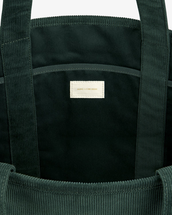 Interior of a dark green Large Corduroy Unisphere Tote Bag featuring a central fabric label with gold lettering.