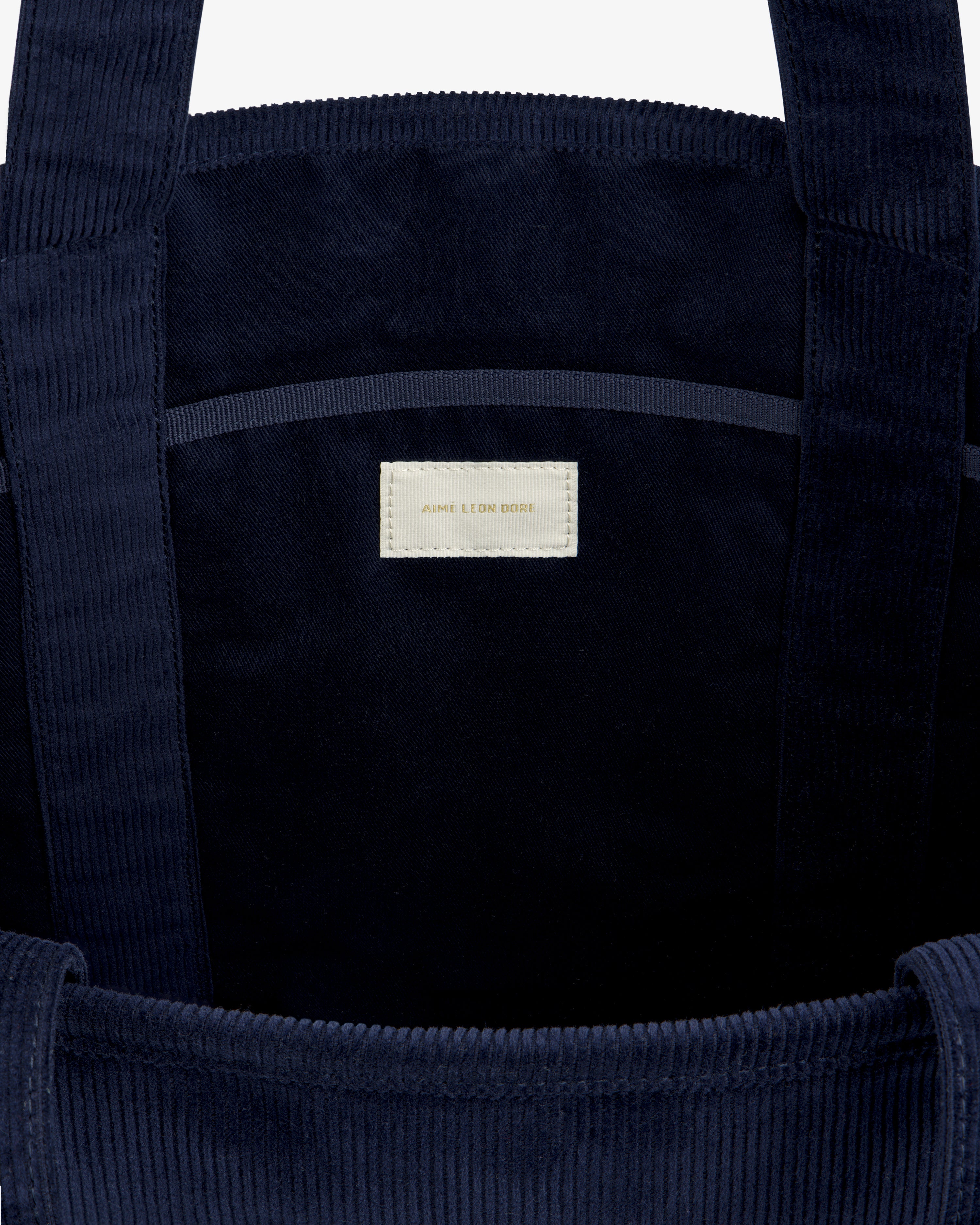 Inside a dark blue Large Corduroy Unisphere Tote Bag featuring a central fabric label with AIME LEON DORE text.