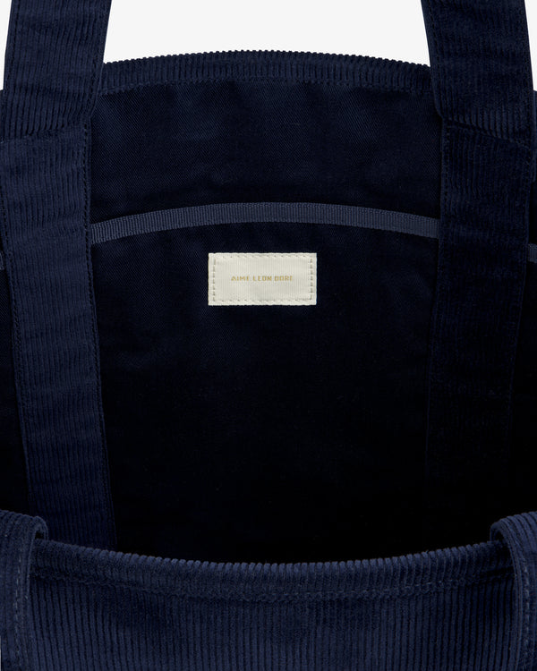 Inside a dark blue Large Corduroy Unisphere Tote Bag featuring a central fabric label with AIME LEON DORE text.