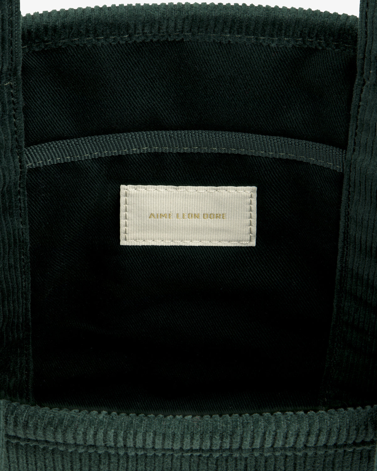Interior of a dark green Mini Corduroy Unisphere Tote Bag with a central AIME LEON DORE fabric label in gold text.