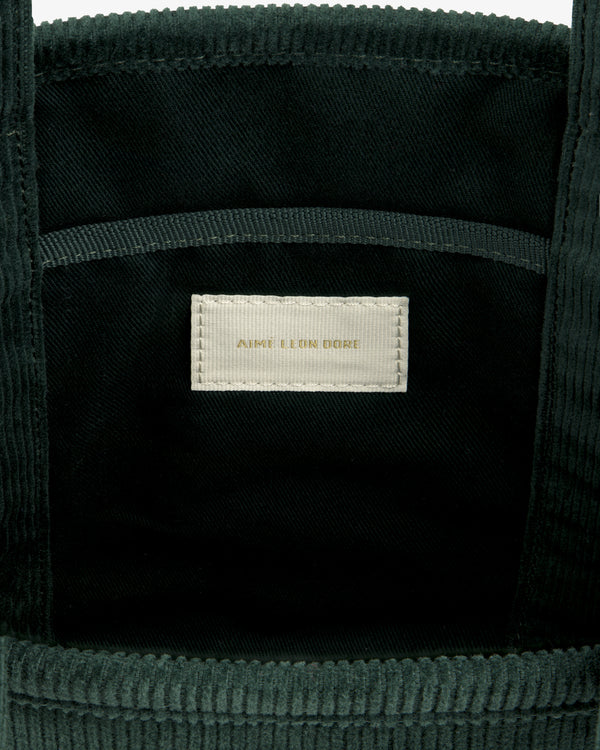 Interior of a dark green Mini Corduroy Unisphere Tote Bag with a central AIME LEON DORE fabric label in gold text.