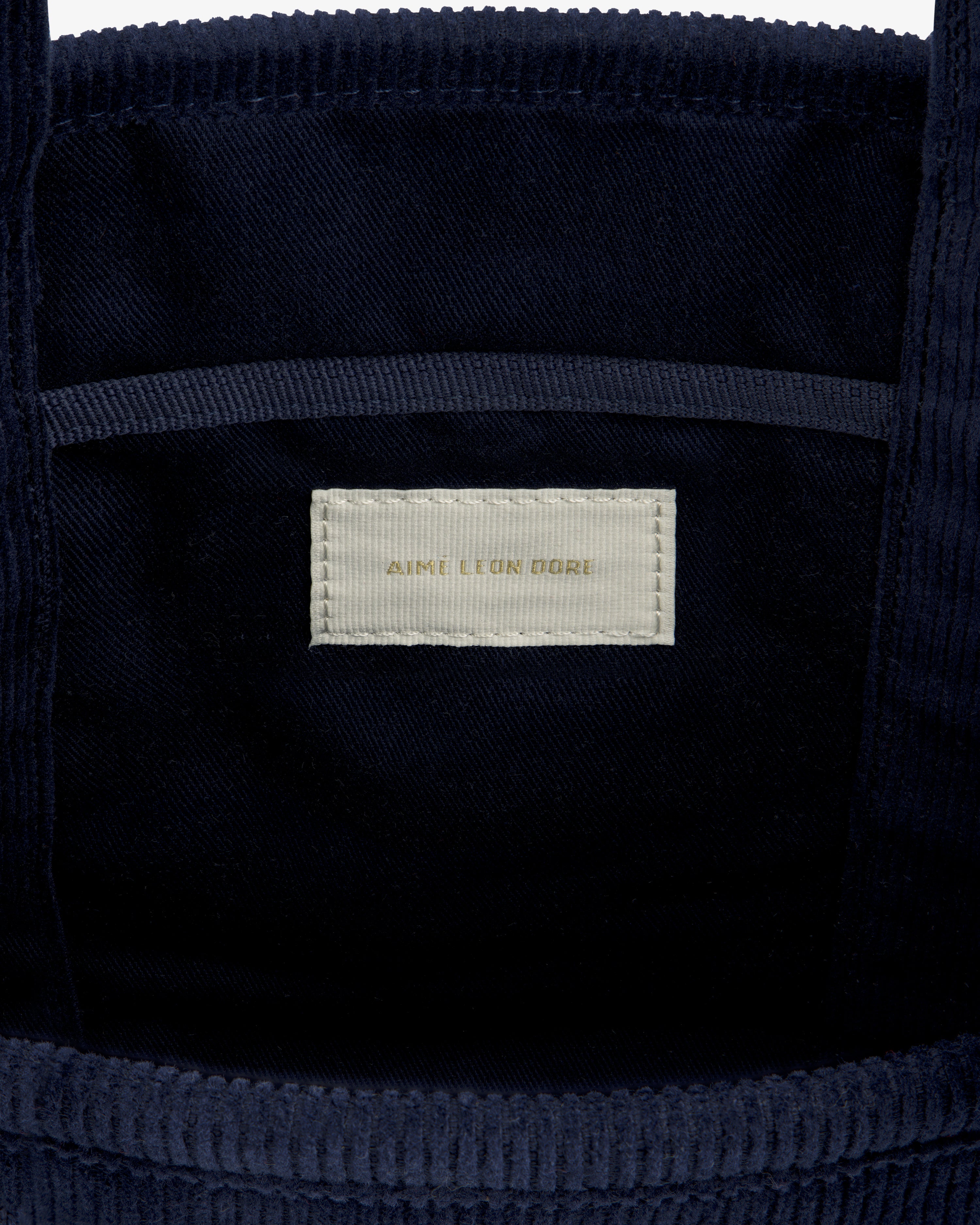 Interior of a navy Mini Corduroy Unisphere Tote Bag showing a beige rectangular label that reads Aime Leon Dore.