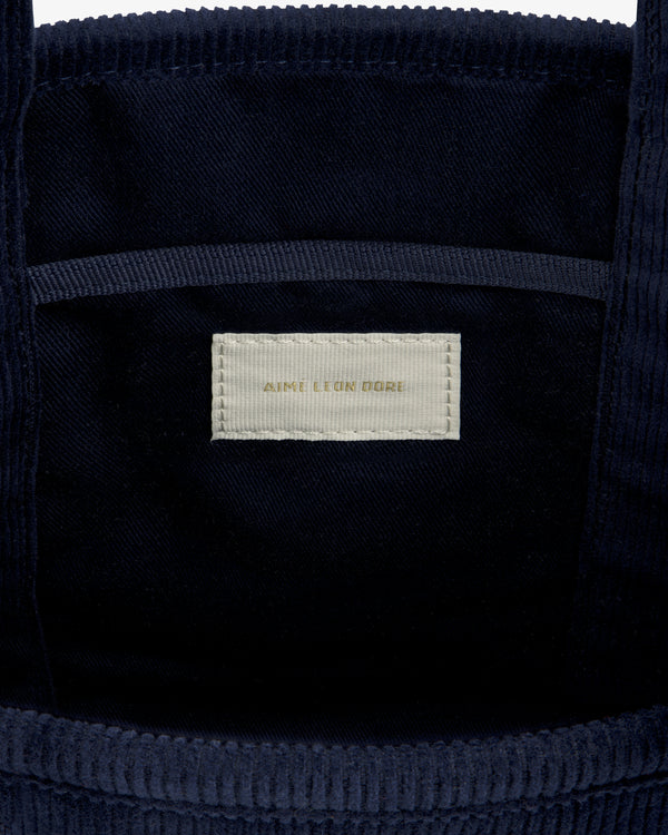 Interior of a navy Mini Corduroy Unisphere Tote Bag showing a beige rectangular label that reads Aime Leon Dore.