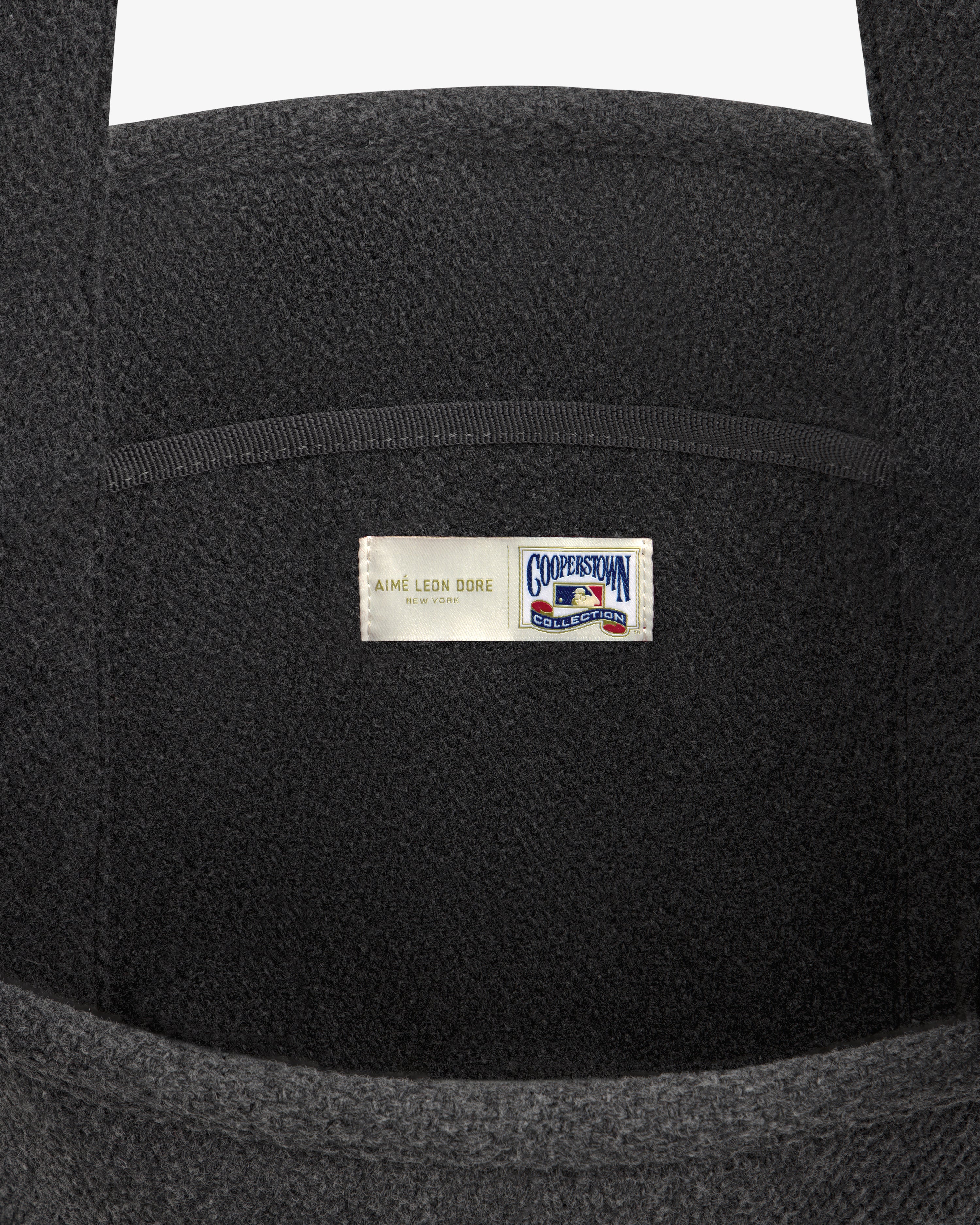 Close-up of a dark gray NY Highlanders Wool Tote Bag with a centered Aimé Leon Dore and Cooperstown Collection label.