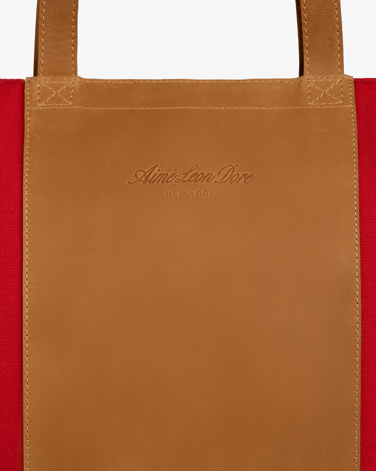 Close-up of a tan leather patch embossed with branding on red canvas, from the Leather Canvas Zip Tote.