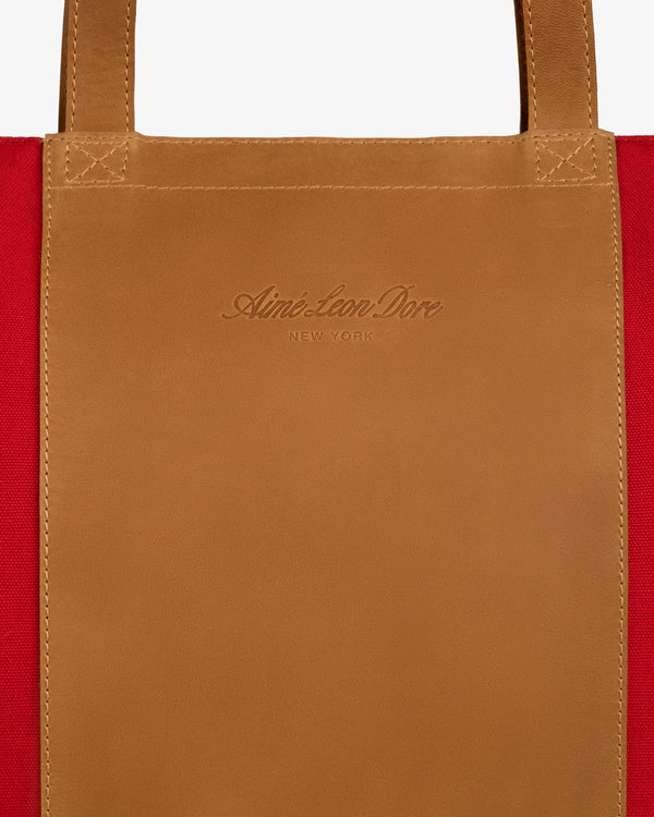 Close-up of a tan leather patch embossed with branding on red canvas, from the Leather Canvas Zip Tote.