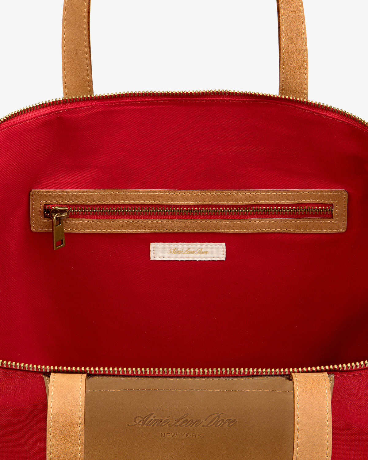 Open Leather Canvas Zip Tote in tan with red interior, visible zip pocket, and fabric label below the zipper.