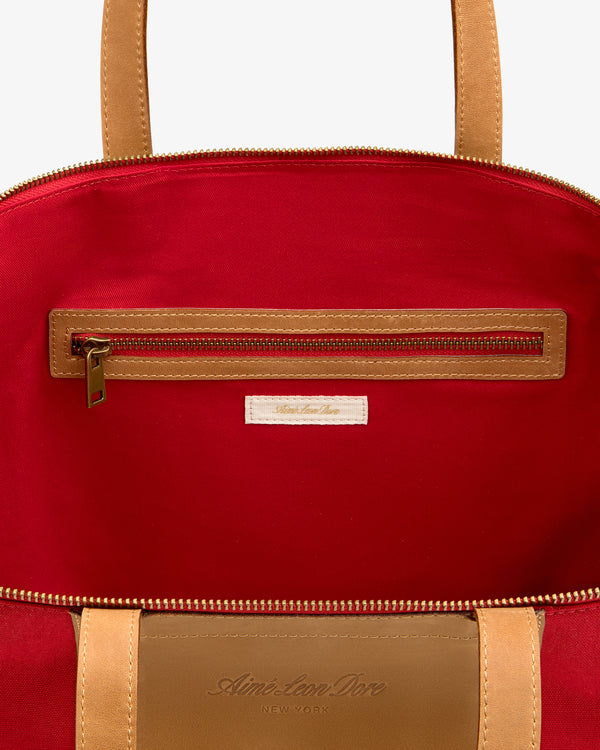 Open Leather Canvas Zip Tote in tan with red interior, visible zip pocket, and fabric label below the zipper.