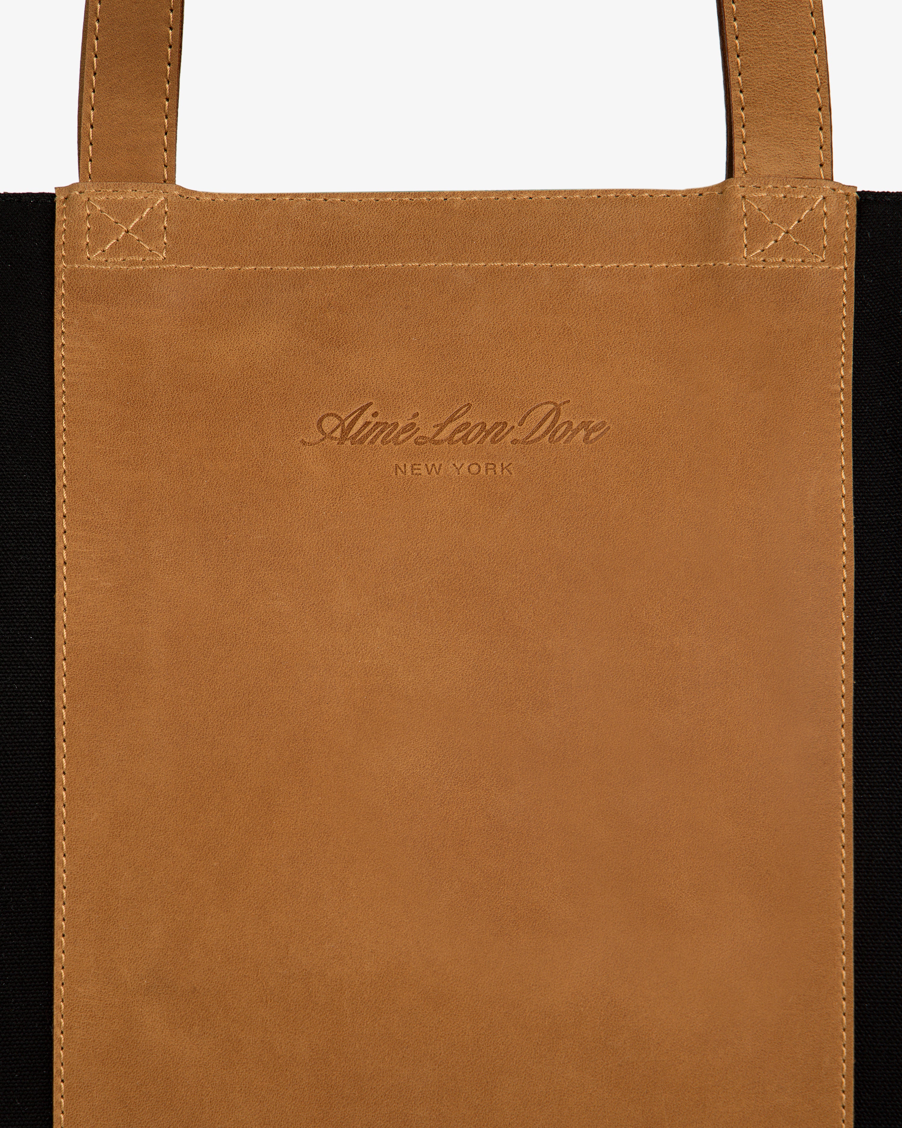 Close-up of a brown Leather Canvas Zip Tote with Aimé Leon Dore NEW YORK embossed on the front panel.