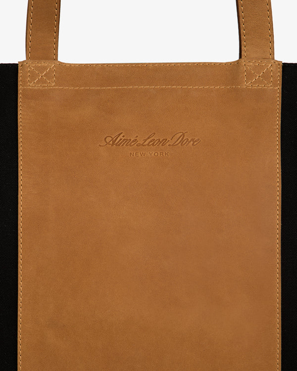 Close-up of a brown Leather Canvas Zip Tote with Aimé Leon Dore NEW YORK embossed on the front panel.