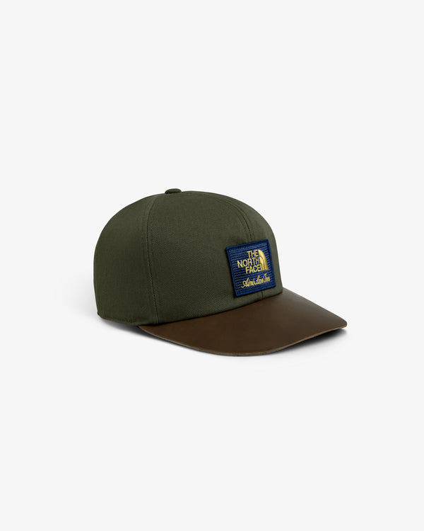 ALD / The North Face Leather Brim Logo Hat in dark green with a brown leather brim and blue patch, on white background.