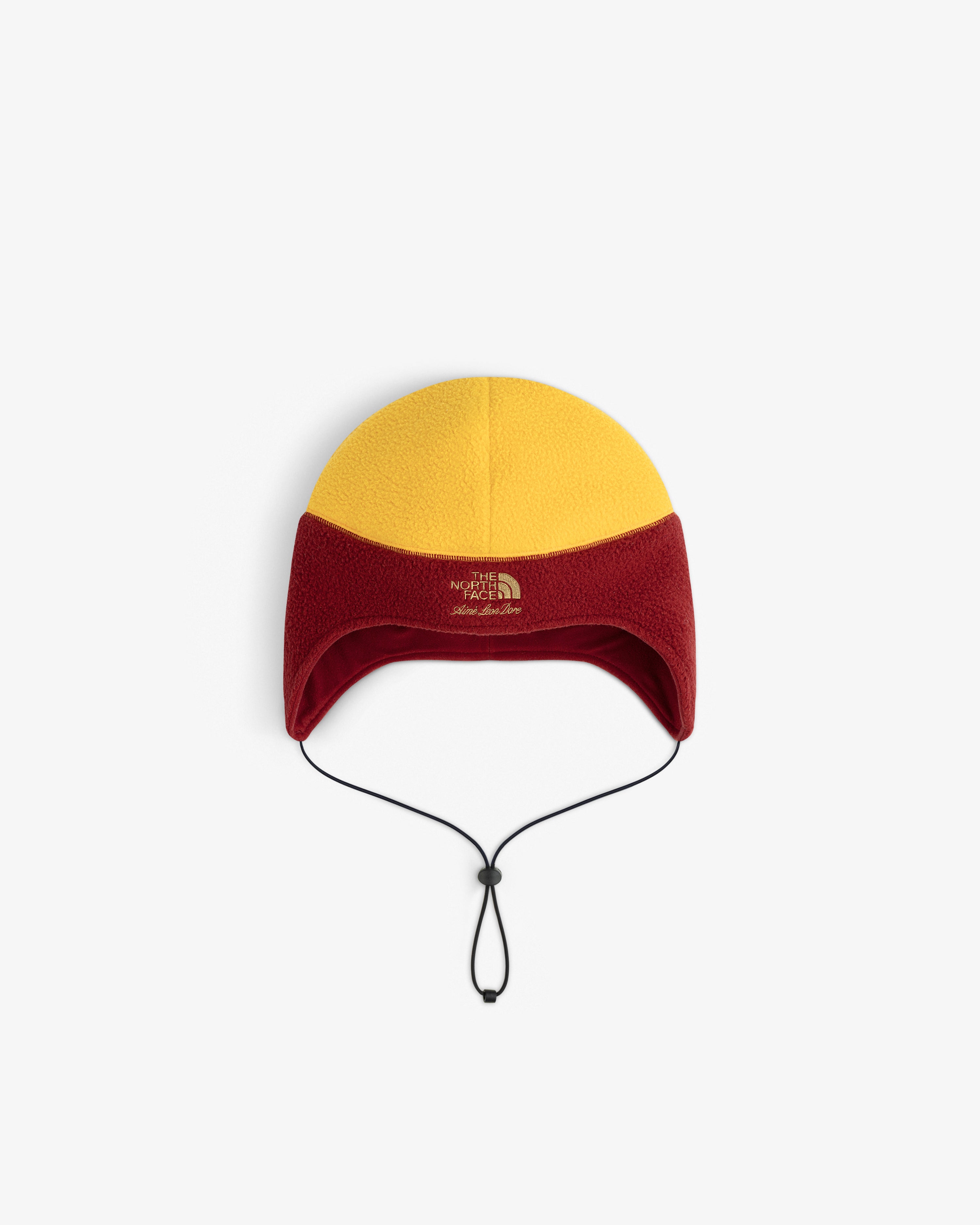 ALD / The North Face Fleece Earflap Hat in yellow and red, with ear flaps, chin strap, and logo on front.