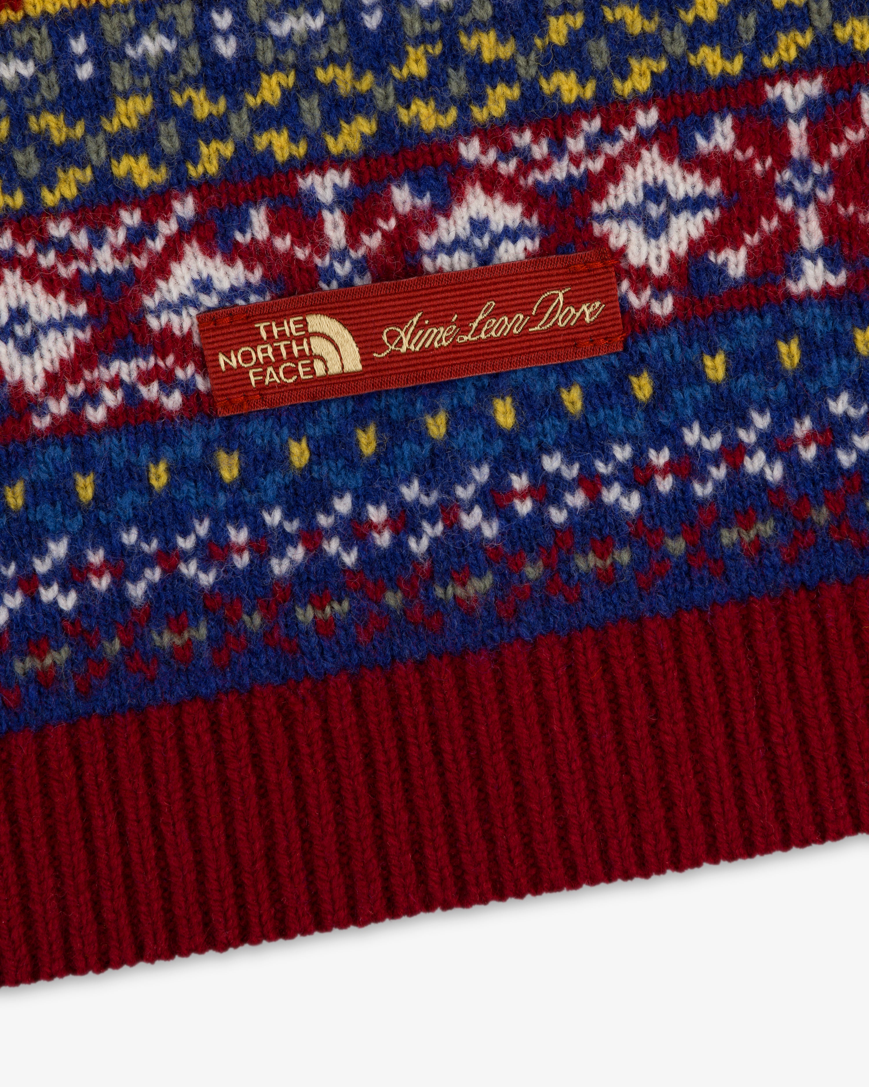 Close-up of the ALD / The North Face Fair Isle Balaclava with a brown co-branded tag on patterned knit fabric.